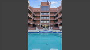 Outdoor swimming pool with blue tile coping and a brick apartment building featuring multiple balconies and large windows