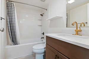 Bathroom with a white tub-shower combination, bronze shower fixtures, a dark wood-finish vanity with a white countertop, and a brass faucet