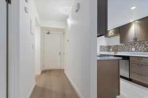 Entryway with wood-finish flooring and white baseboards, opening to a kitchen featuring dark cabinetry, a mosaic tile backsplash, and a gold-tone faucet