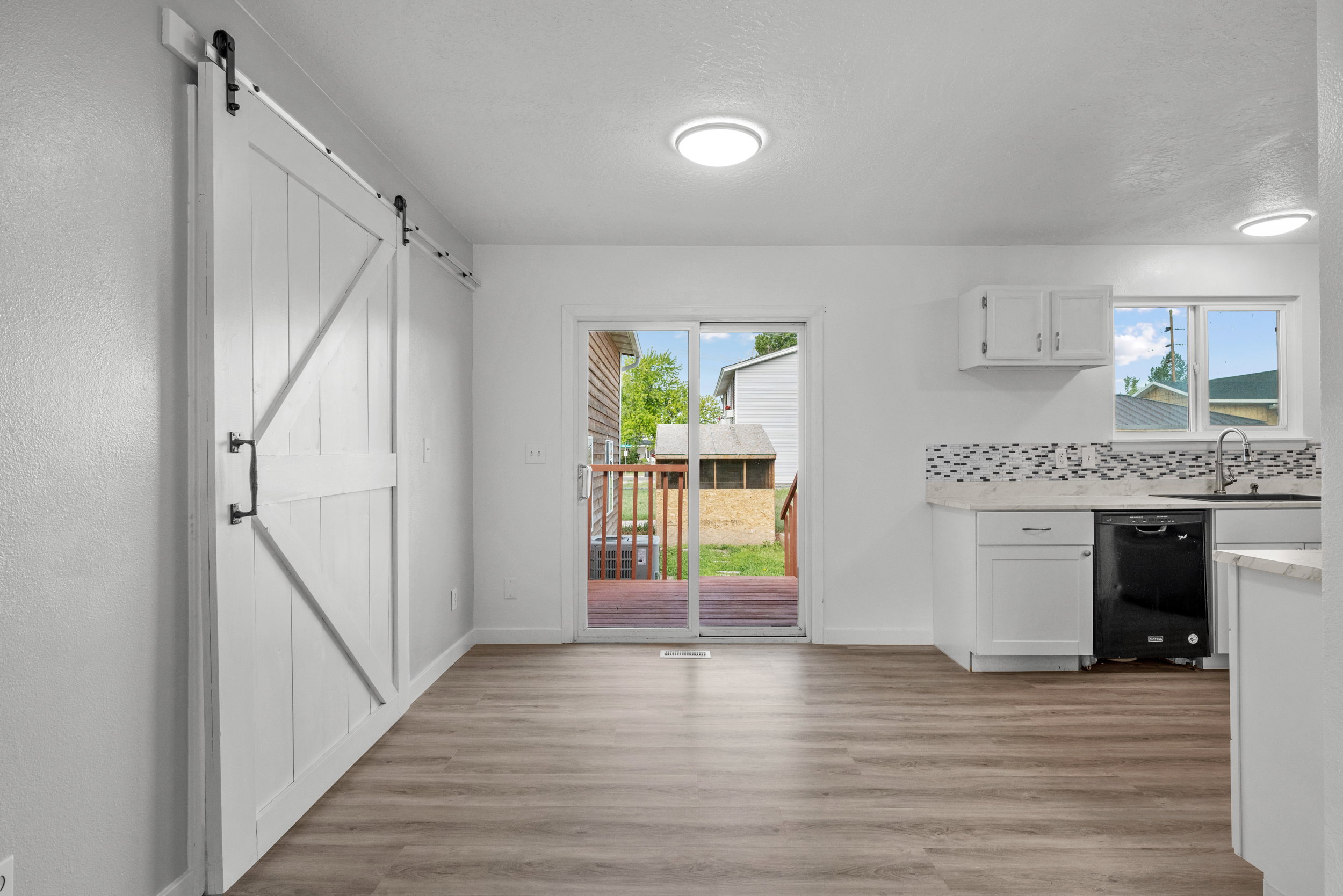 Open-concept living area featuring wood-finish flooring, a contemporary white barn door, and sliding glass doors opening to an outdoor deck