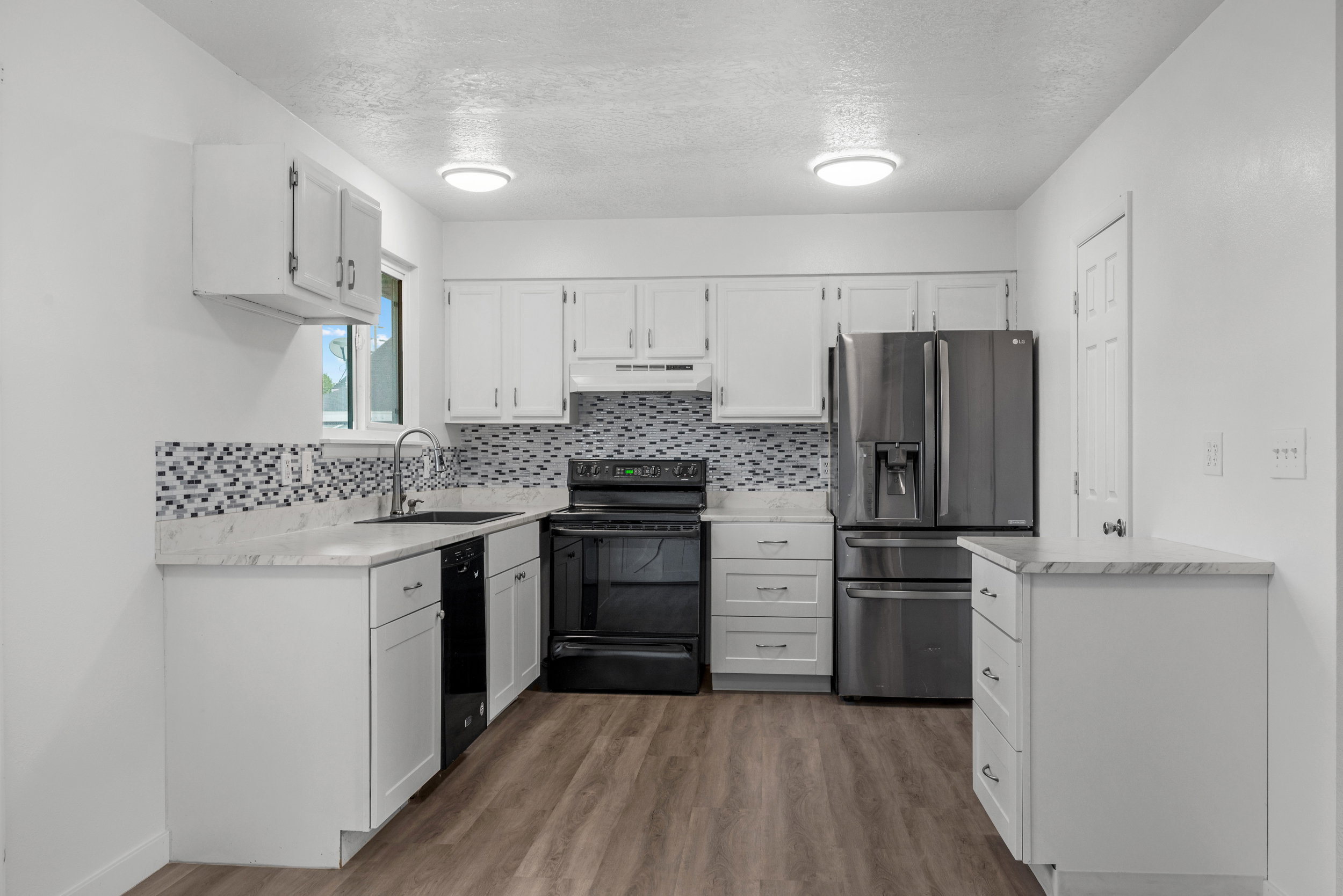 Kitchen featuring white cabinetry, wood-finish flooring, stainless steel refrigerator, black range, and mosaic tile backsplash