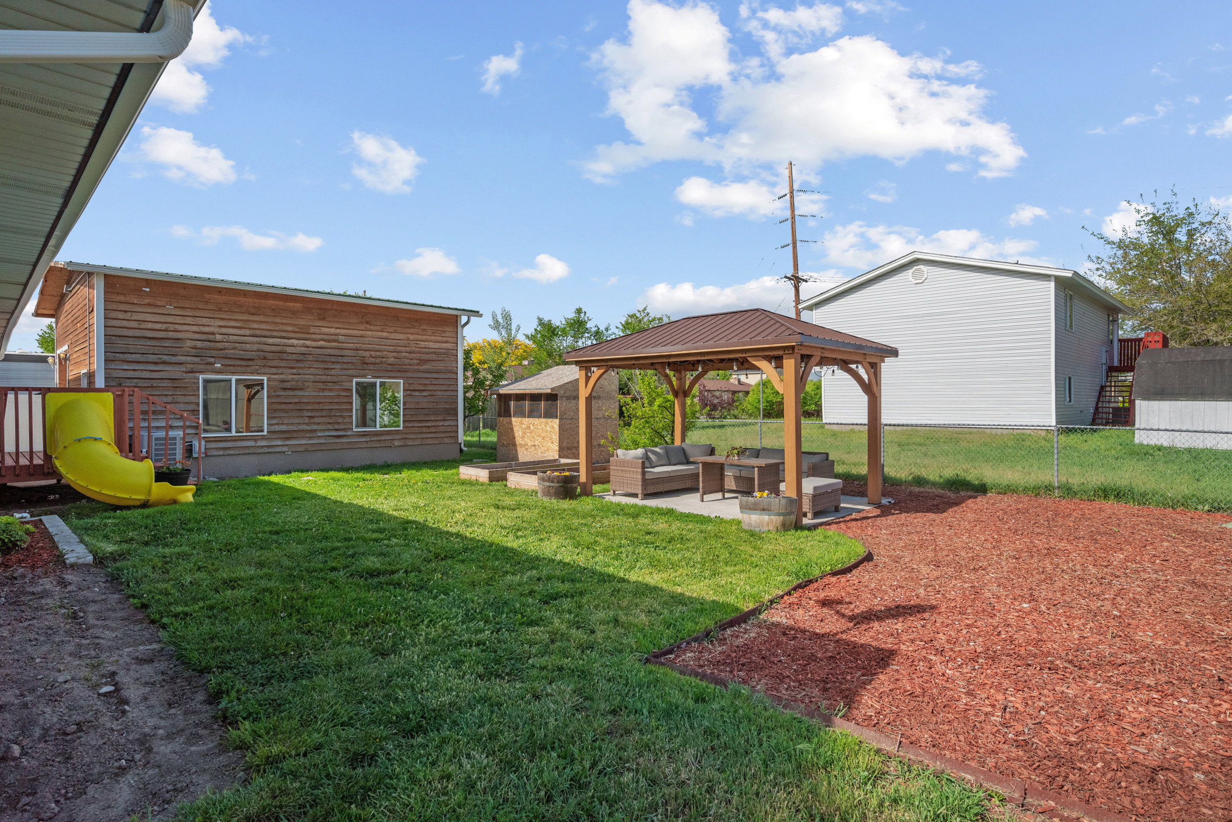 Backyard featuring a gazebo with a metal roof, an adjacent concrete patio, and a separate wood chip area