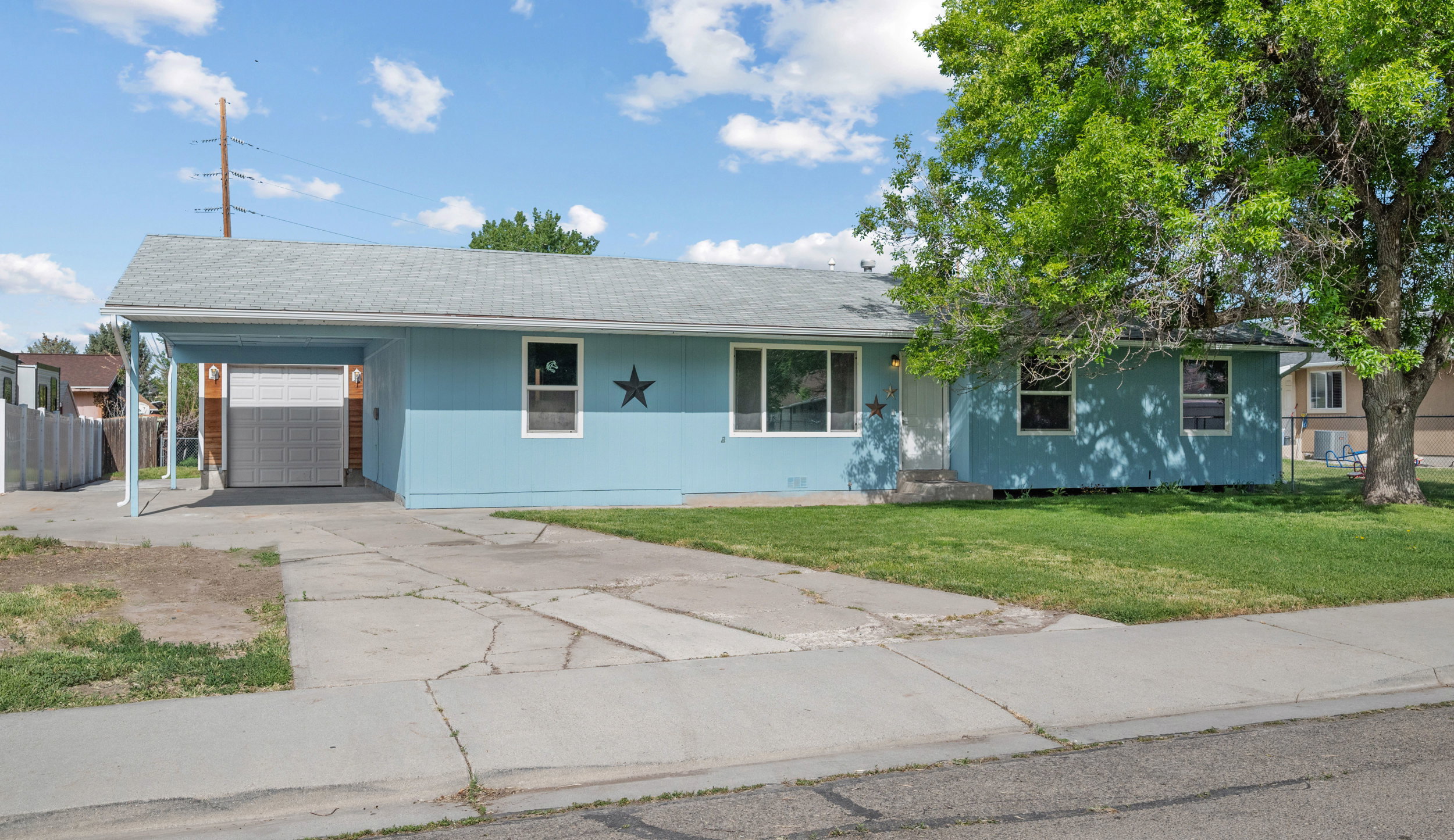 Single-story residence featuring a carport, attached garage, concrete driveway, and a front lawn with mature trees
