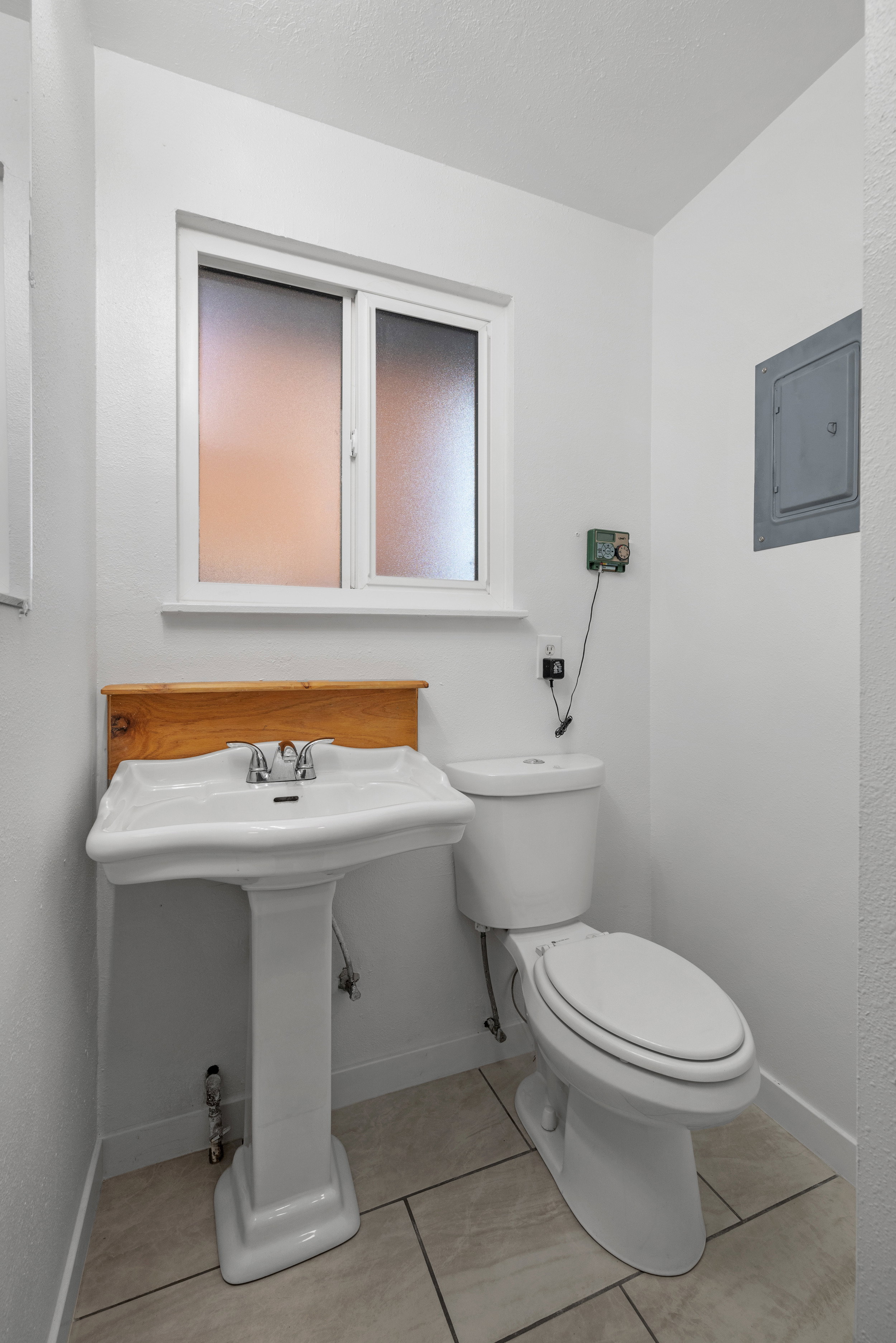 Pedestal sink with chrome faucet, white toilet, and frosted window