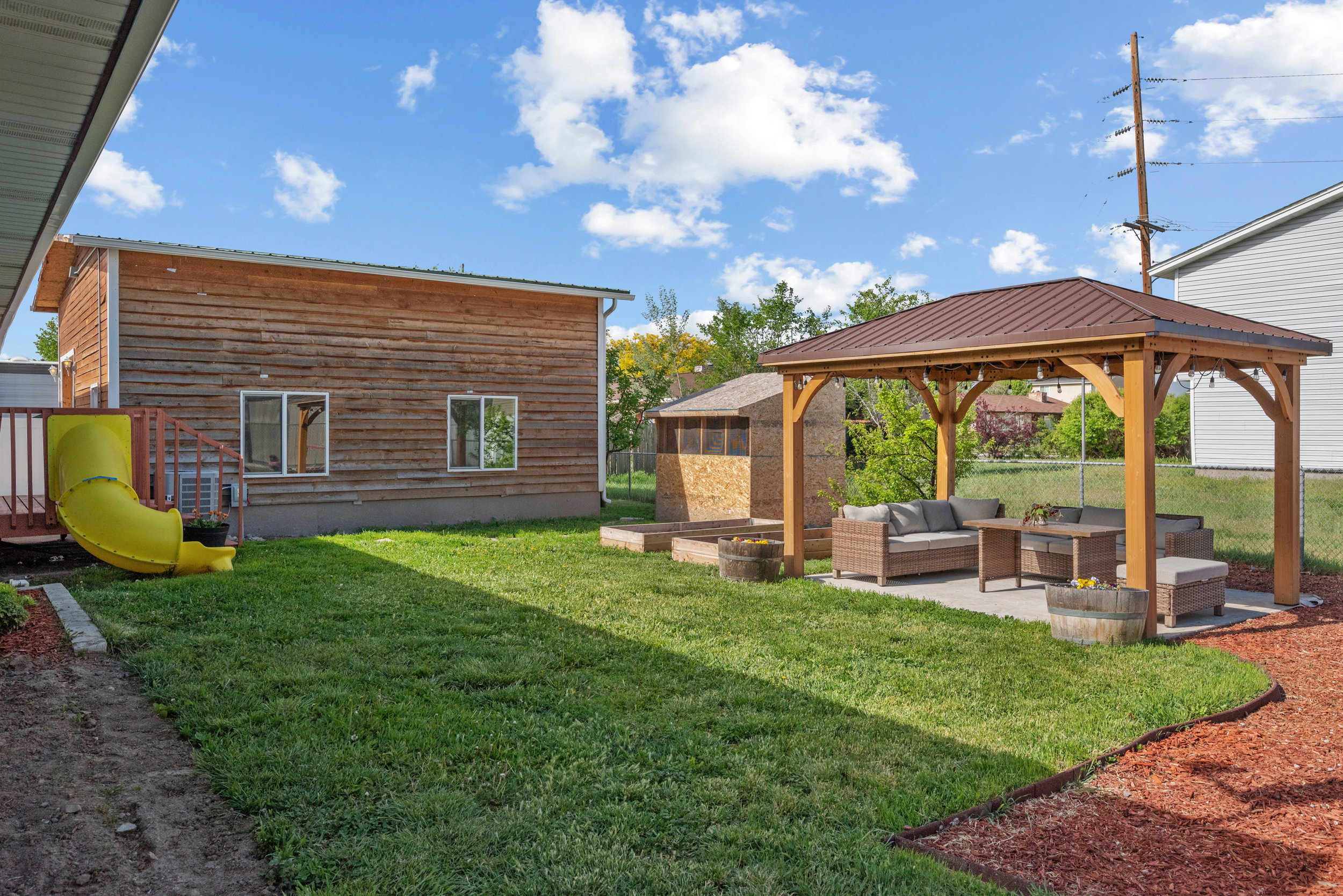 Expansive backyard featuring a large lawn, a wooden gazebo with a metal roof over a concrete patio, and a wooden accessory structure