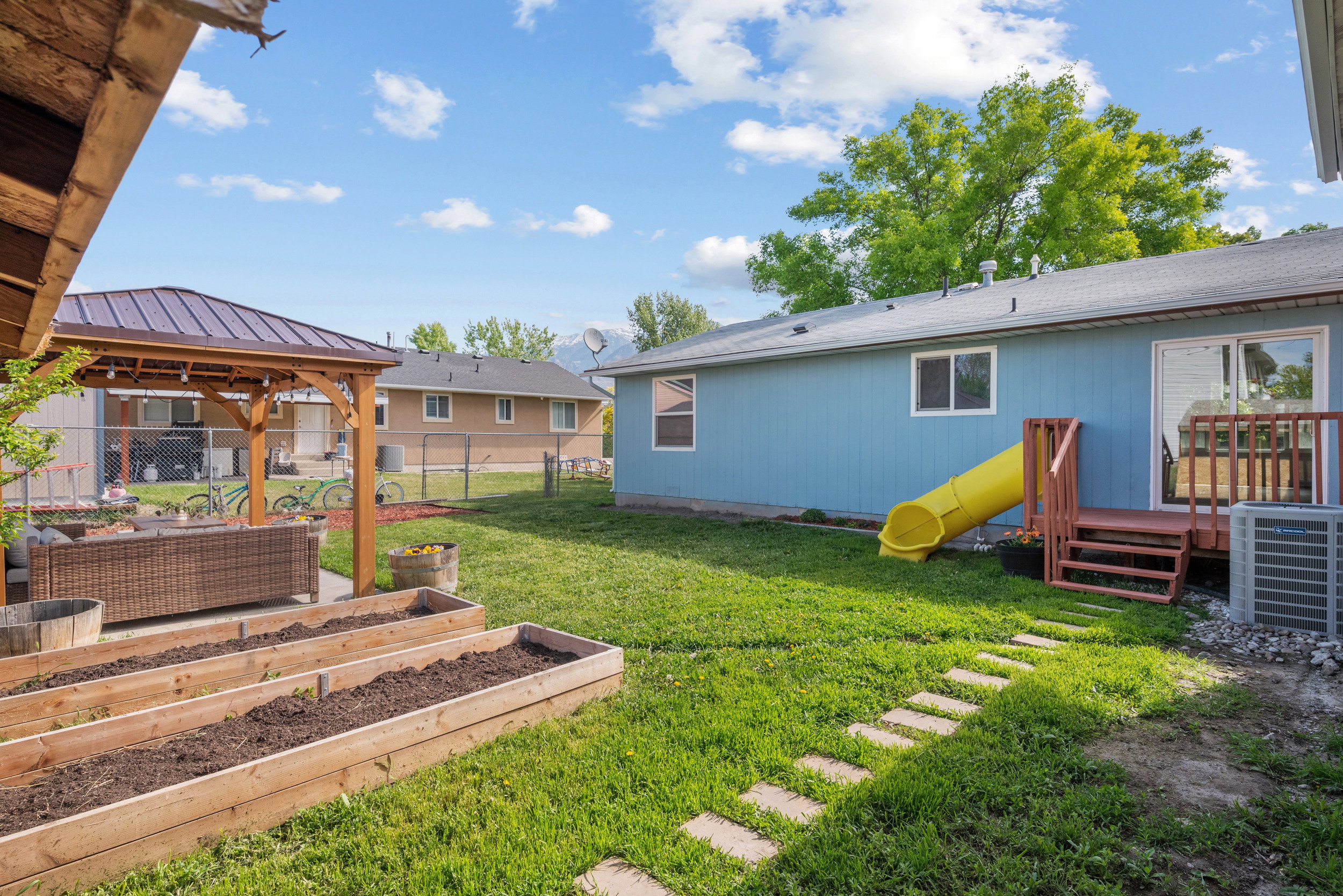 Expansive backyard featuring a covered patio, raised garden beds, a wooden deck, and a sliding glass door entry to the home