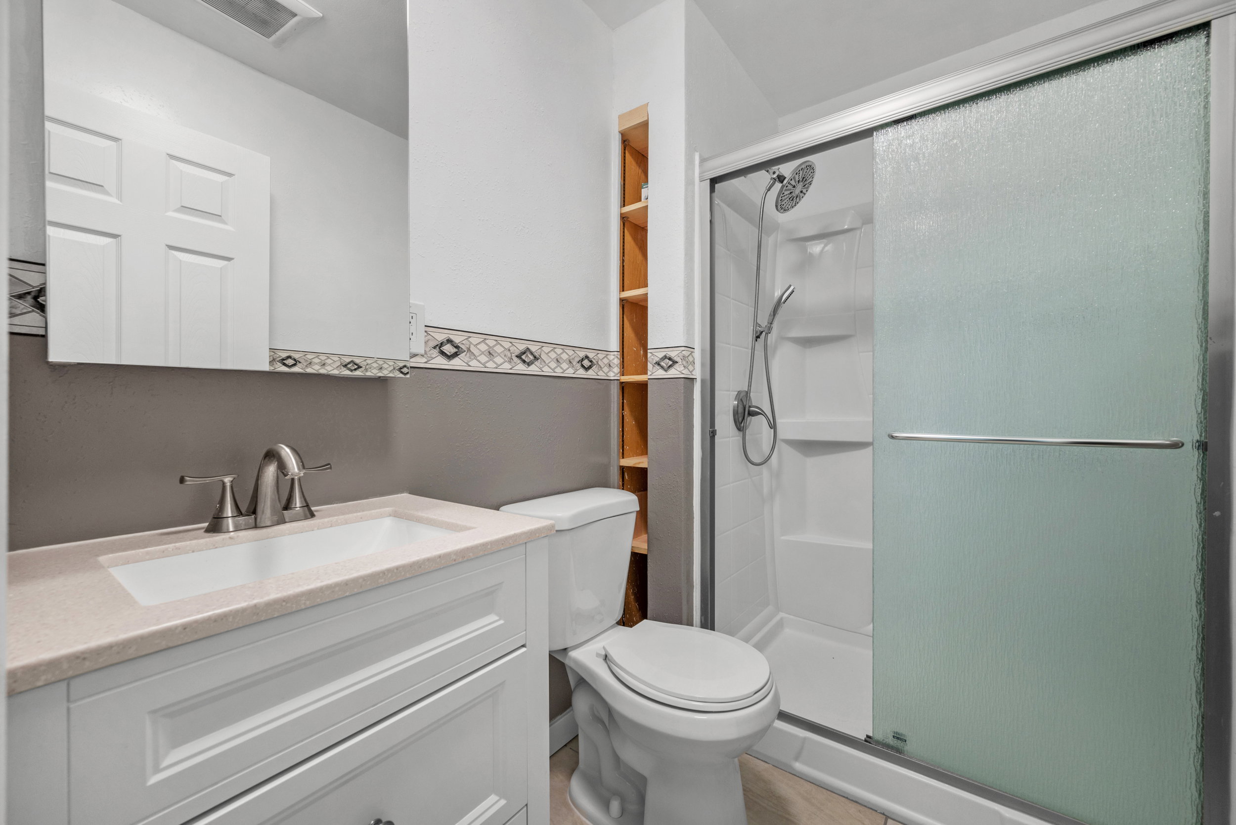 Bathroom featuring a white vanity with a light-toned countertop, a shower with sliding frosted glass doors, and built-in shelving
