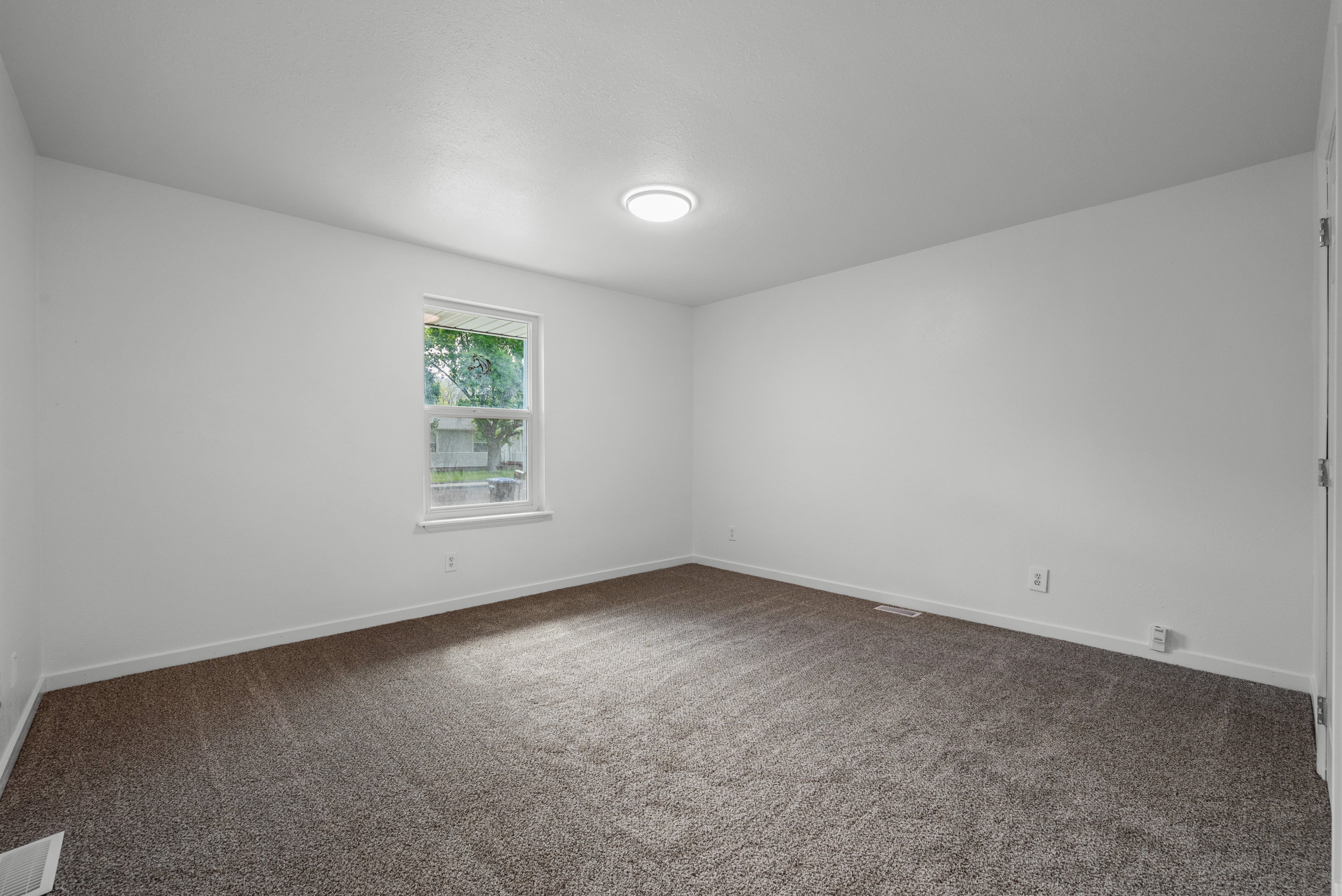 Neutral white wall paint with a single window, overhead flush-mount lighting, and wall-to-wall carpeting