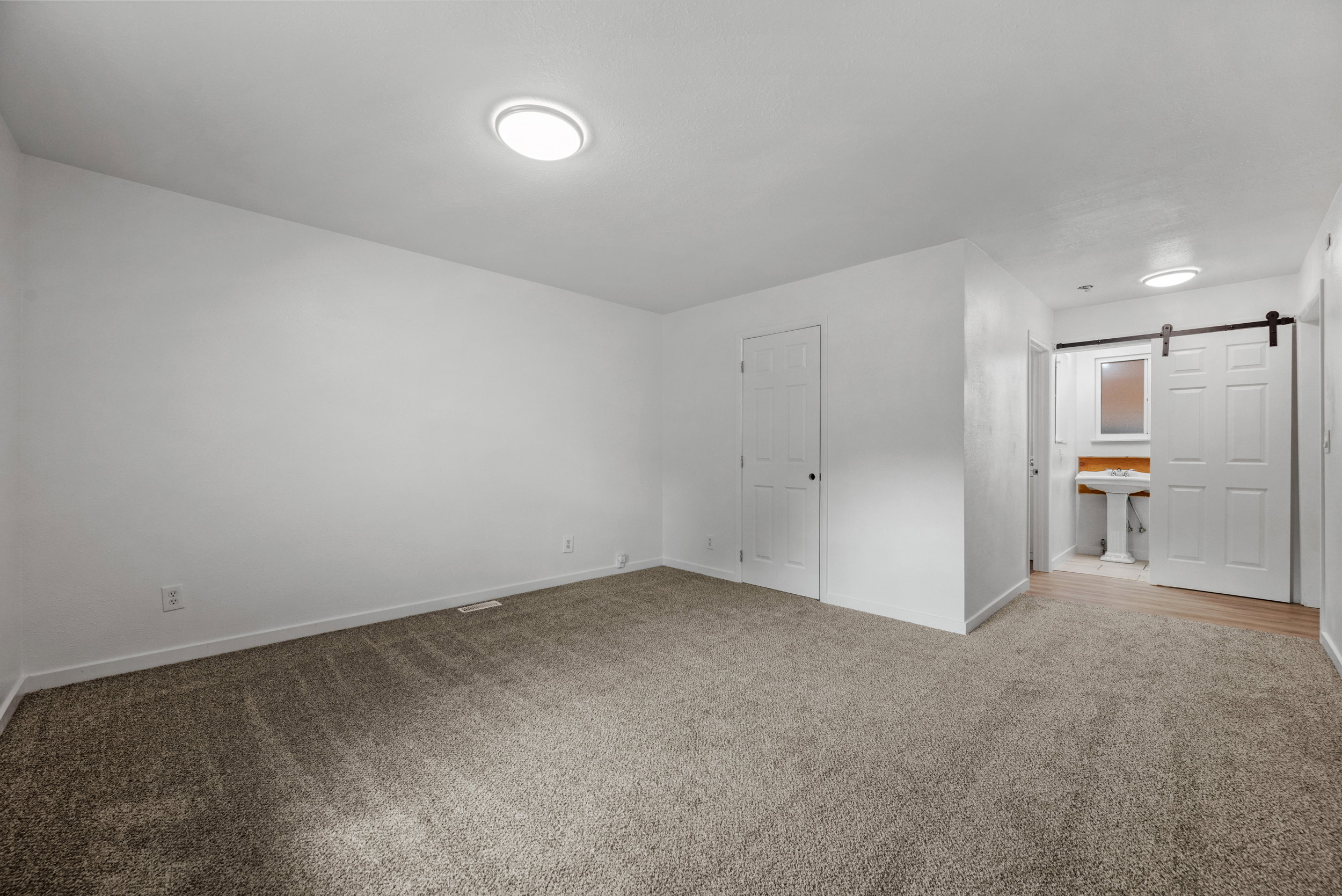 Carpeted room with white walls, ceiling-mounted lighting, and a white interior door