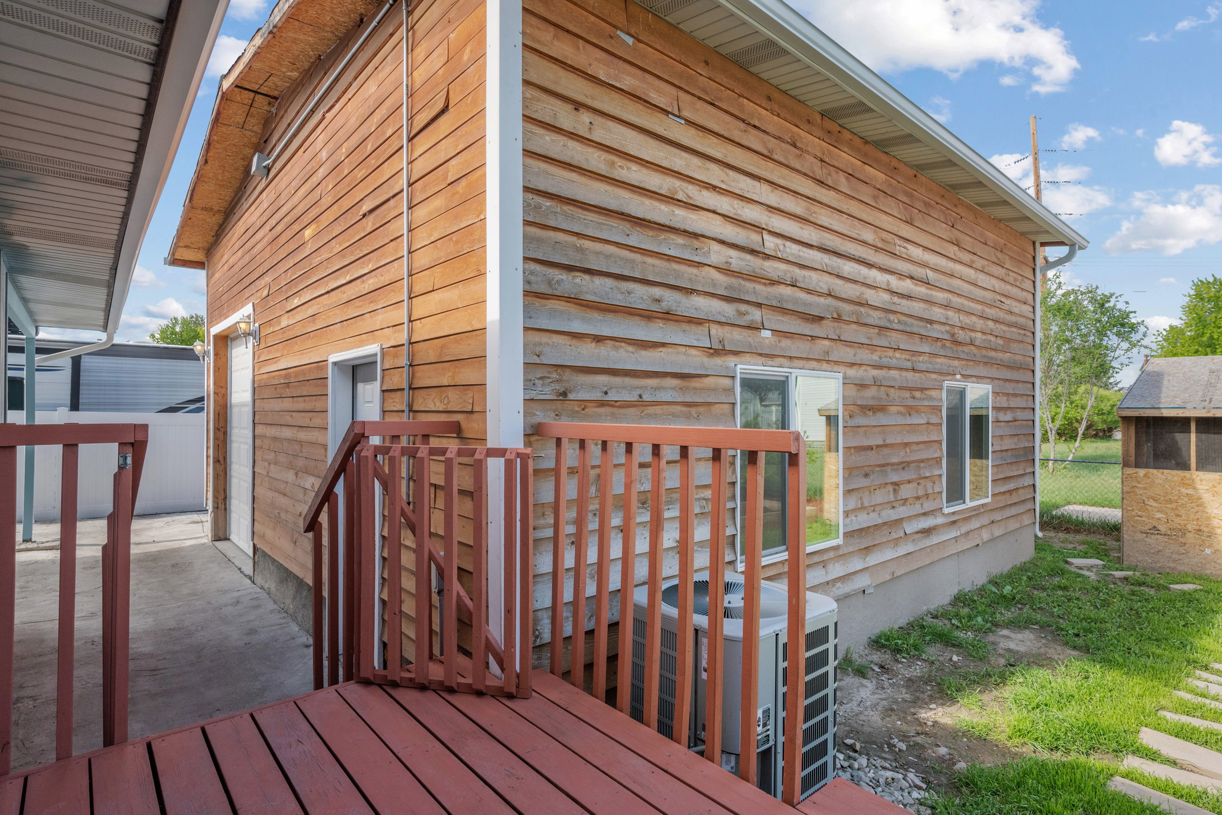 Exterior featuring wood plank siding, multiple windows, and a red-stained wooden deck