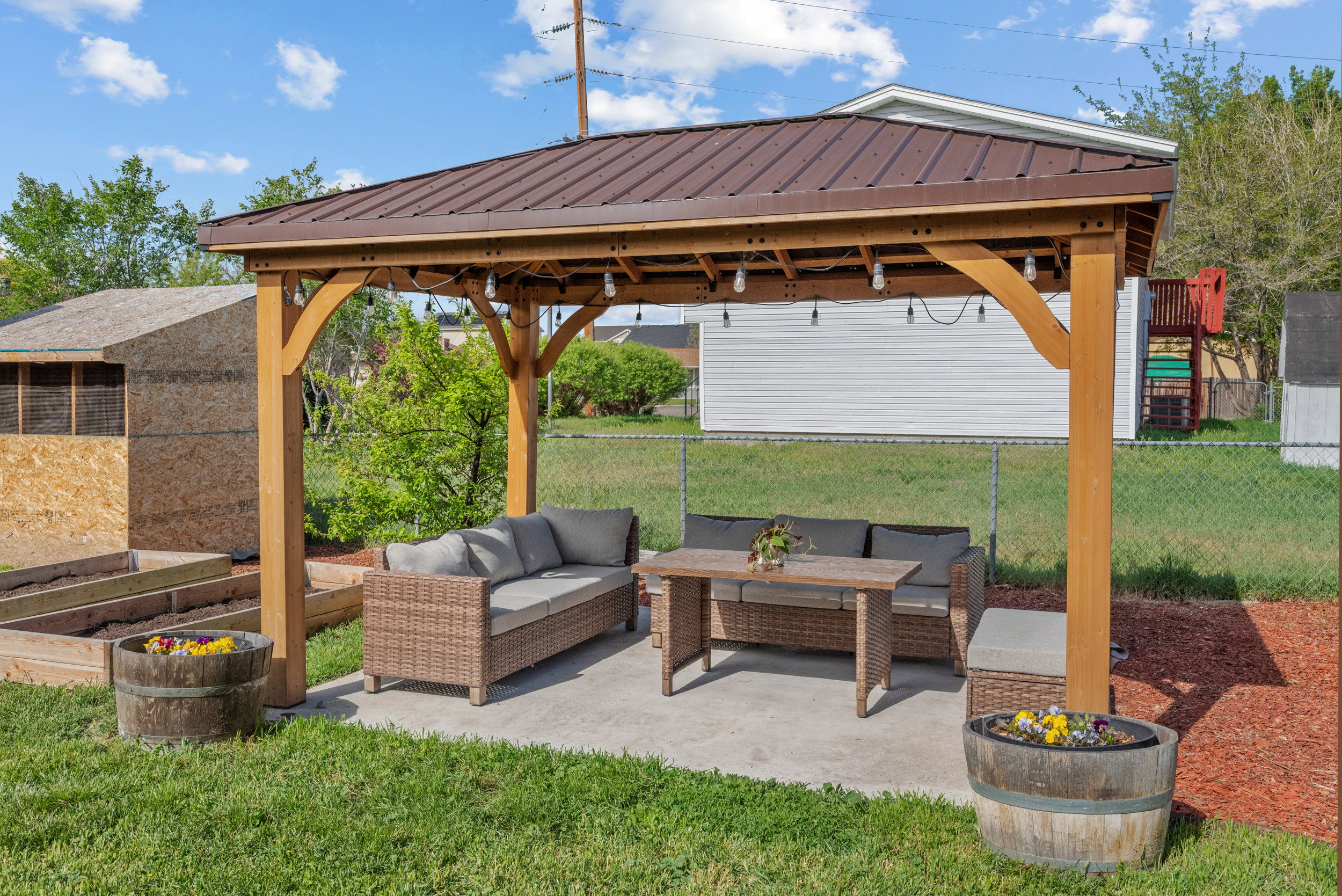 Outdoor patio featuring a wooden gazebo with a metal roof, string lighting, and a concrete pad
