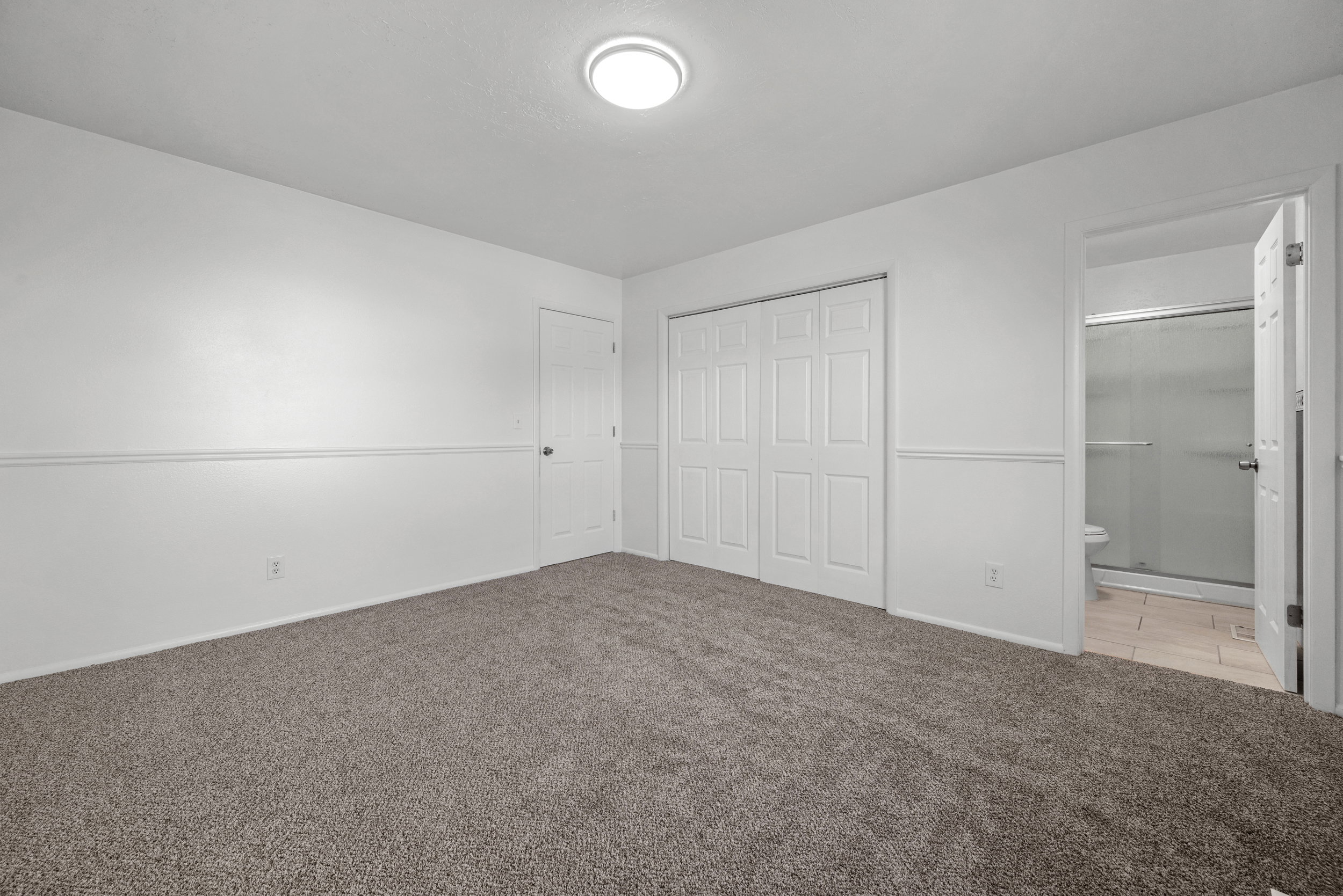 Carpeted room featuring a ceiling-mounted light fixture, white walls with wainscoting, and a white bi-fold closet door