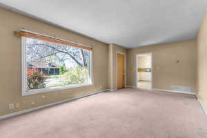 Expansive front room featuring a large picture window, neutral carpeting, and a light beige wall finish