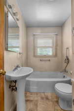 Bathroom featuring a pedestal sink, white bathtub, and light-colored flooring