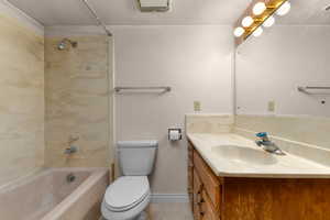 Bathroom featuring a tub/shower combination with patterned wall surround, a white toilet, and a vanity with a light-toned countertop and wood-finish cabinetry