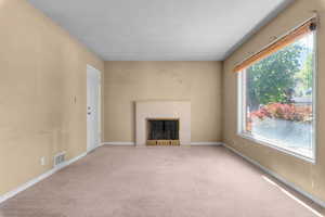 Neutral-toned walls and carpeting define this interior space featuring a central fireplace with a light-colored mantel