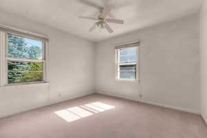 Carpeted room featuring a ceiling fan with light kit, two windows providing natural illumination, and white baseboards