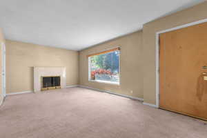 Living area featuring a fireplace with a light-toned mantel, large window with natural light, and carpeting