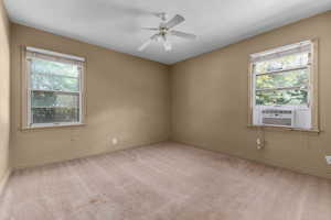 Carpeted room featuring two windows with blinds, a window-mounted air conditioning unit, and a ceiling fan with light fixture