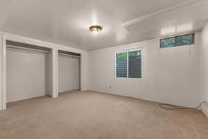 Spacious room featuring neutral carpeting, two open closet spaces with hanging rods, a ceiling-mounted light fixture, and two windows providing natural light