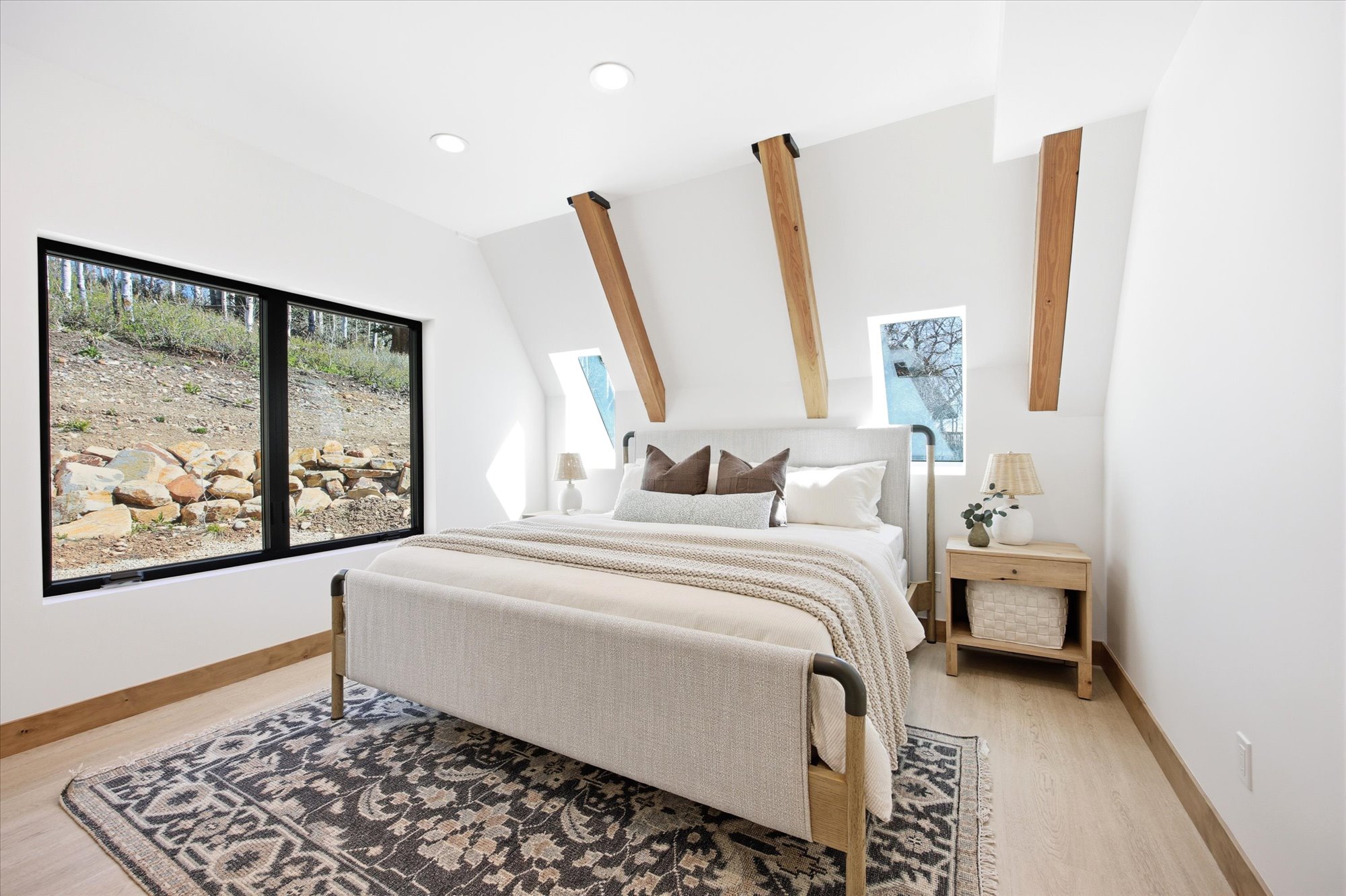 Contemporary bedroom featuring a large picture window, a pair of skylight windows, exposed wooden beams, recessed lighting, and light wood-finish flooring