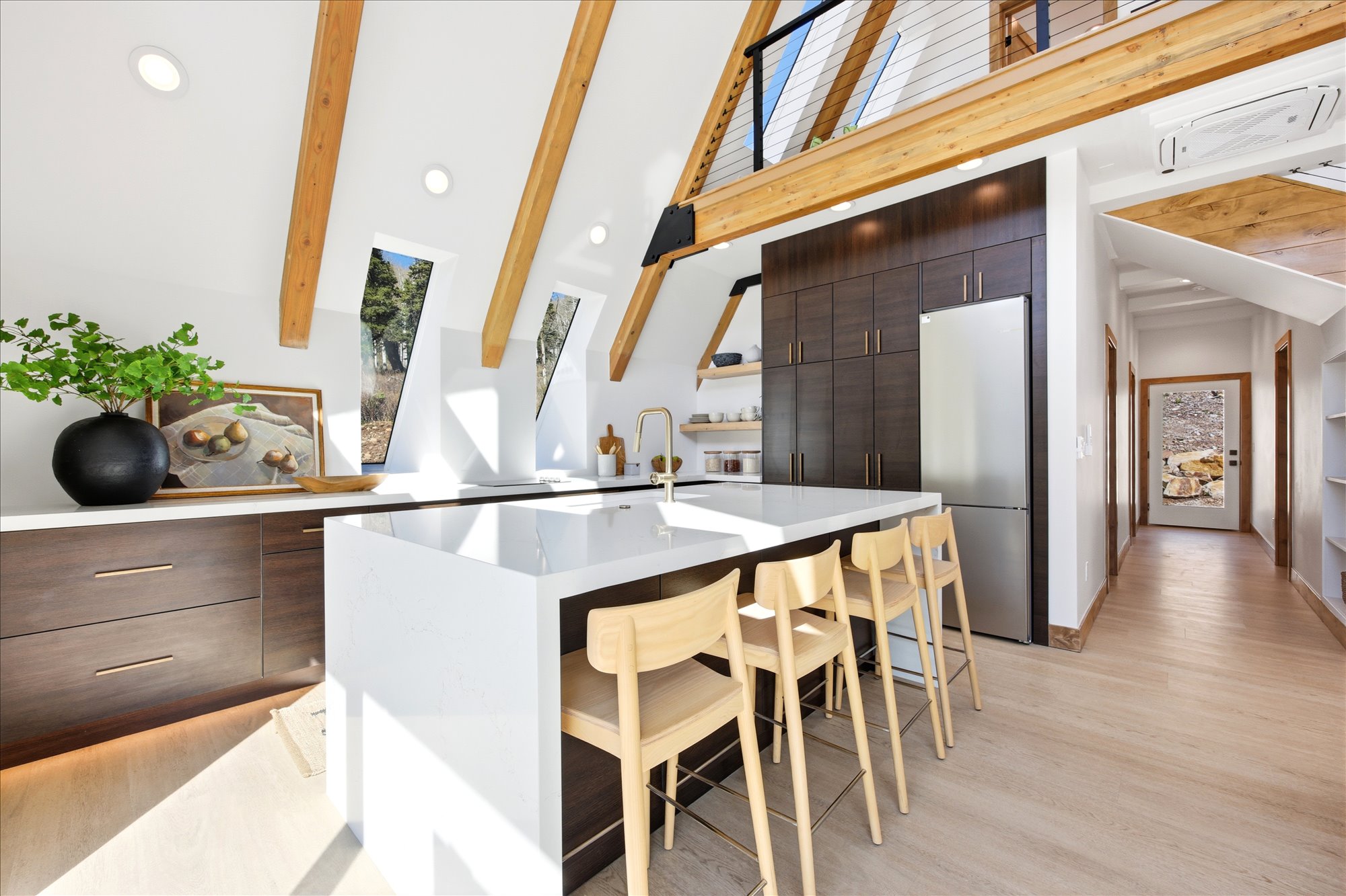 Modern kitchen featuring a large waterfall island with seating, dark wood-finish cabinetry, stainless steel appliances, and integrated shelving