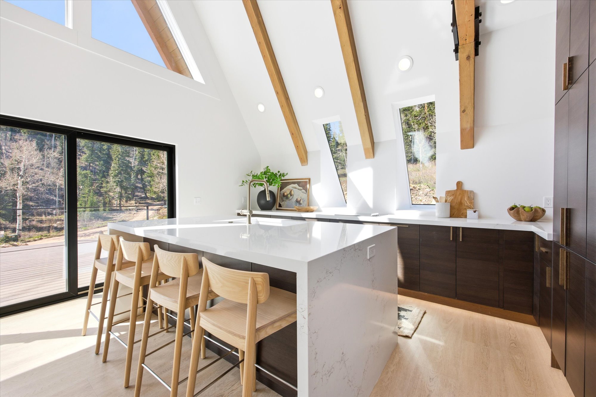 Modern kitchen featuring a waterfall island, light wood-finish flooring, dark wood cabinetry, white countertops, and exposed wood beams