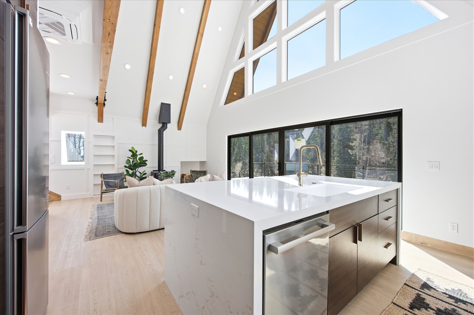 Open-concept interior featuring wood-finish flooring, exposed wood beams, and a modern kitchen island with an integrated sink and gold-tone faucet