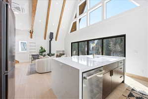 Open-concept interior featuring wood-finish flooring, exposed wood beams, and a modern kitchen island with an integrated sink and gold-tone faucet
