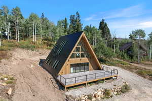A-frame architectural style with a black metal roof, natural wood siding, and an expansive deck featuring a black metal railing