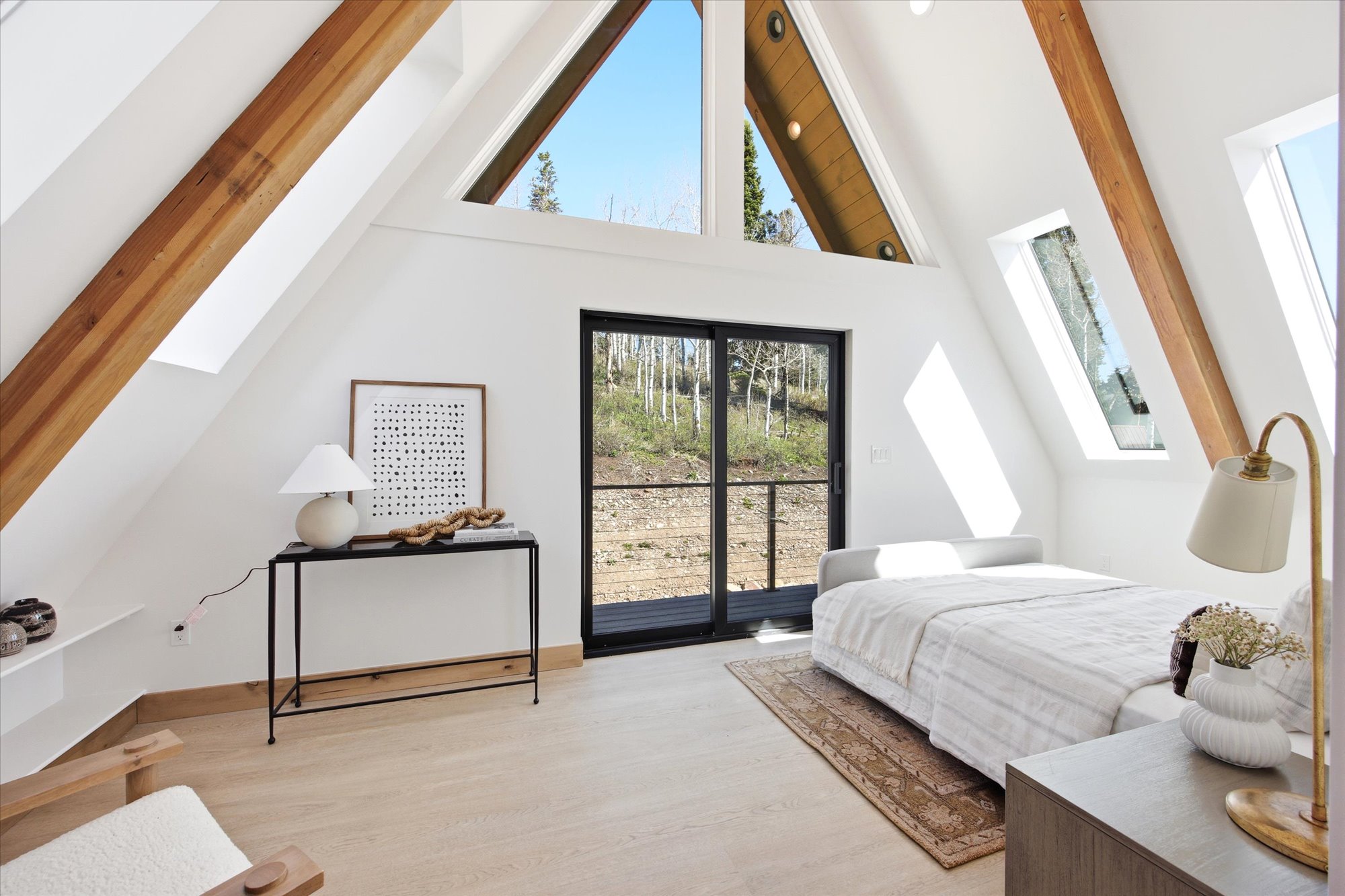 Vaulted ceilings featuring exposed wood beams, expansive windows, and a sliding glass door providing outdoor access