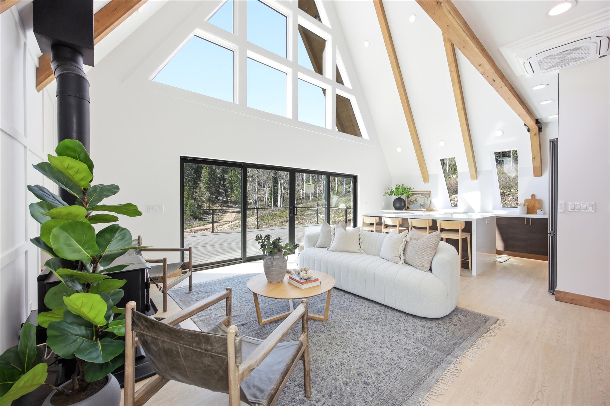 Vaulted ceilings with exposed wood beams define this living area, featuring a prominent wood-burning stove and a wall of floor-to-ceiling windows