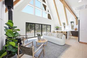 Vaulted ceilings with exposed wood beams define this living area, featuring a prominent wood-burning stove and a wall of floor-to-ceiling windows