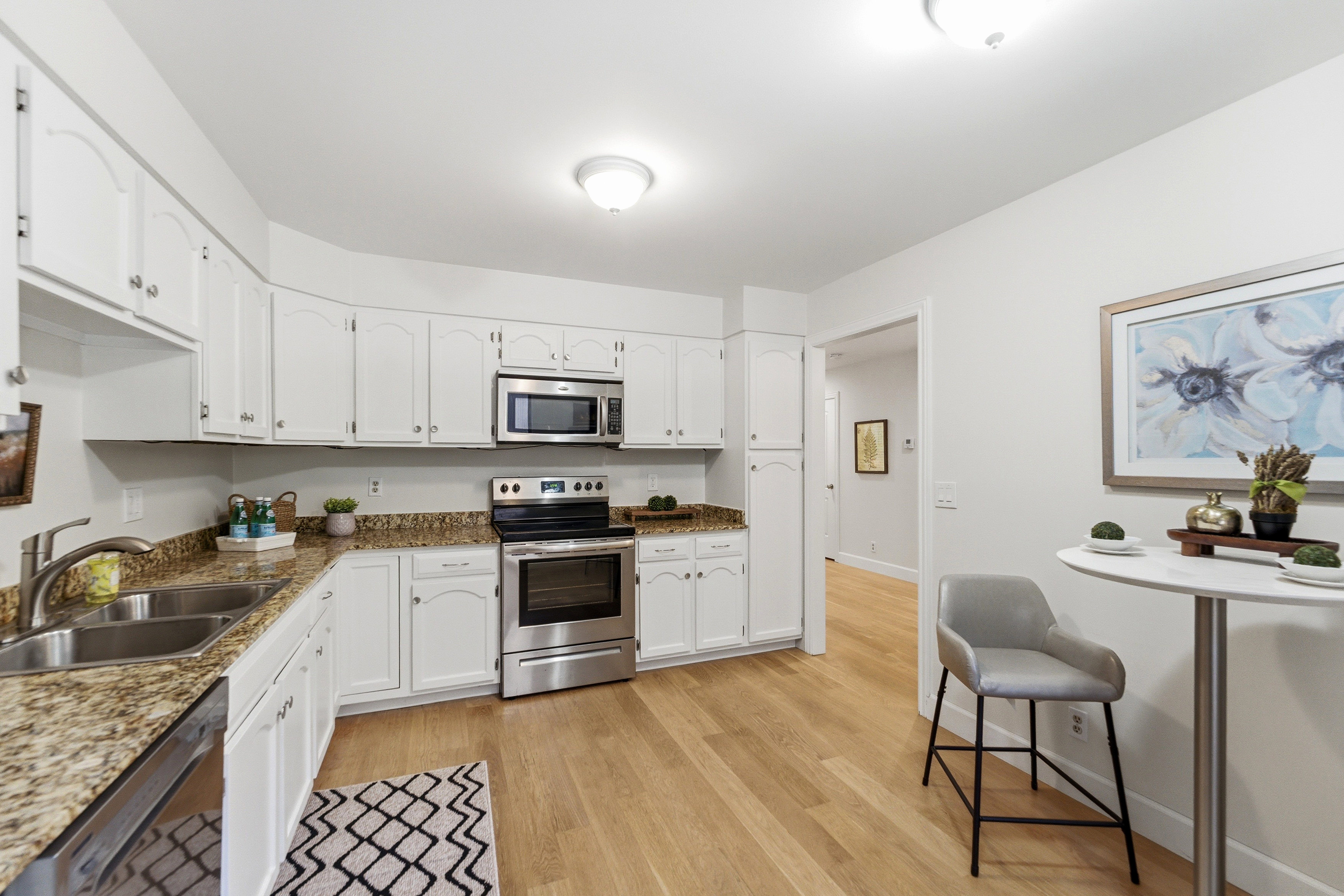 Kitchen featuring white cabinetry, wood-finish flooring, stainless steel appliances, and granite countertops