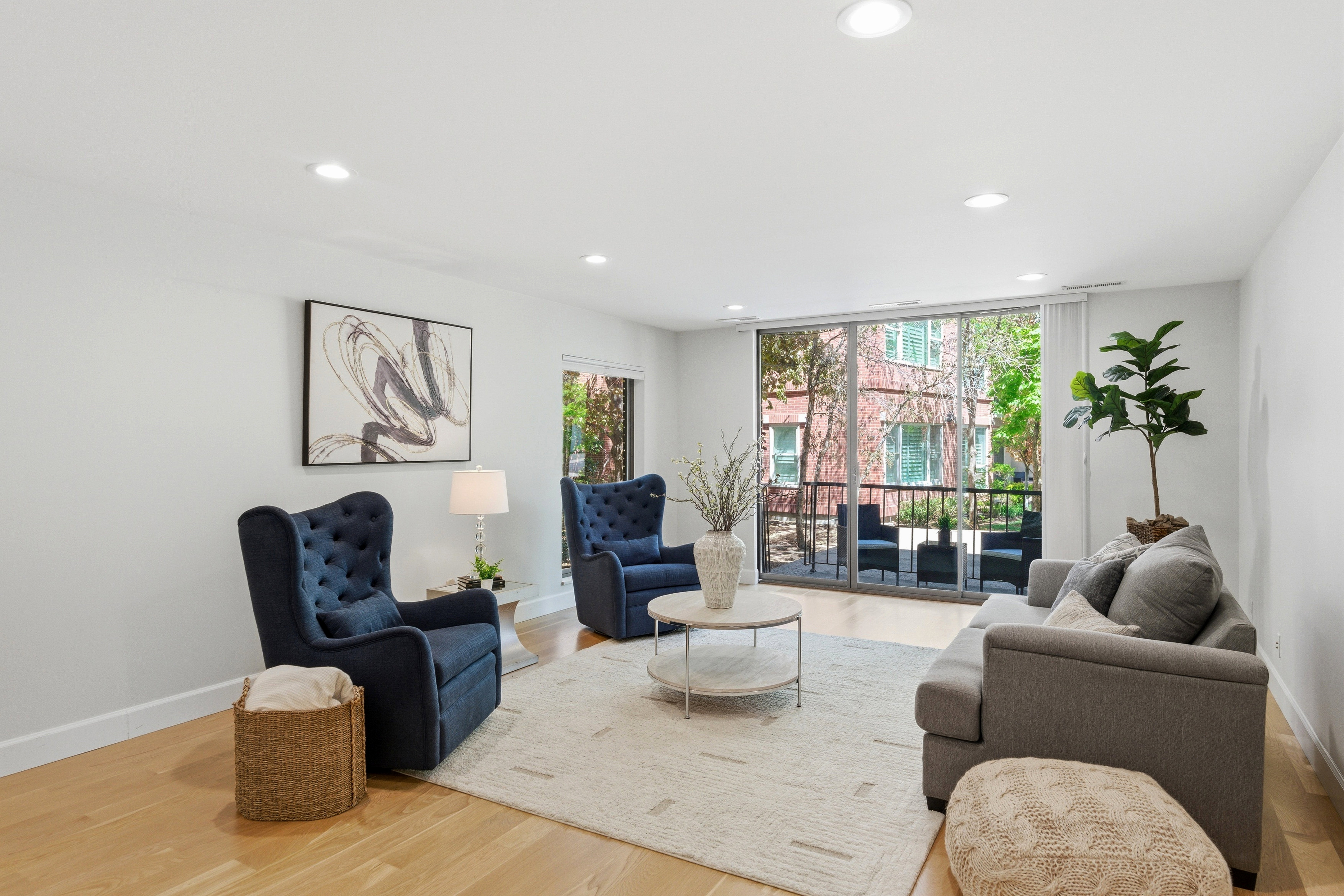 Spacious living area featuring light wood-finish flooring, recessed lighting, and a full wall of glass sliding doors opening to a private balcony