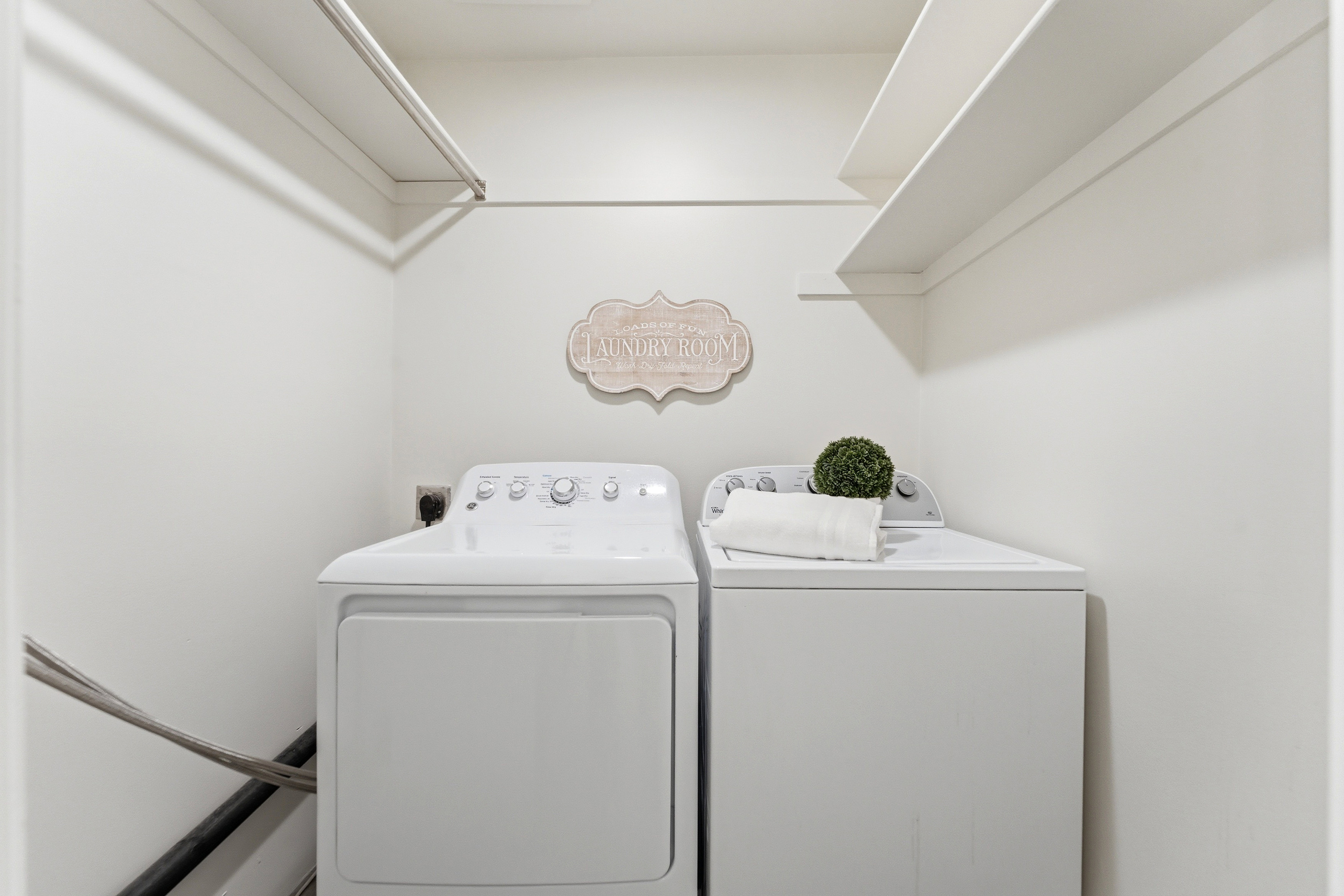 Dedicated laundry area featuring a white color palette, built-in shelving, and a hanging rod for convenience