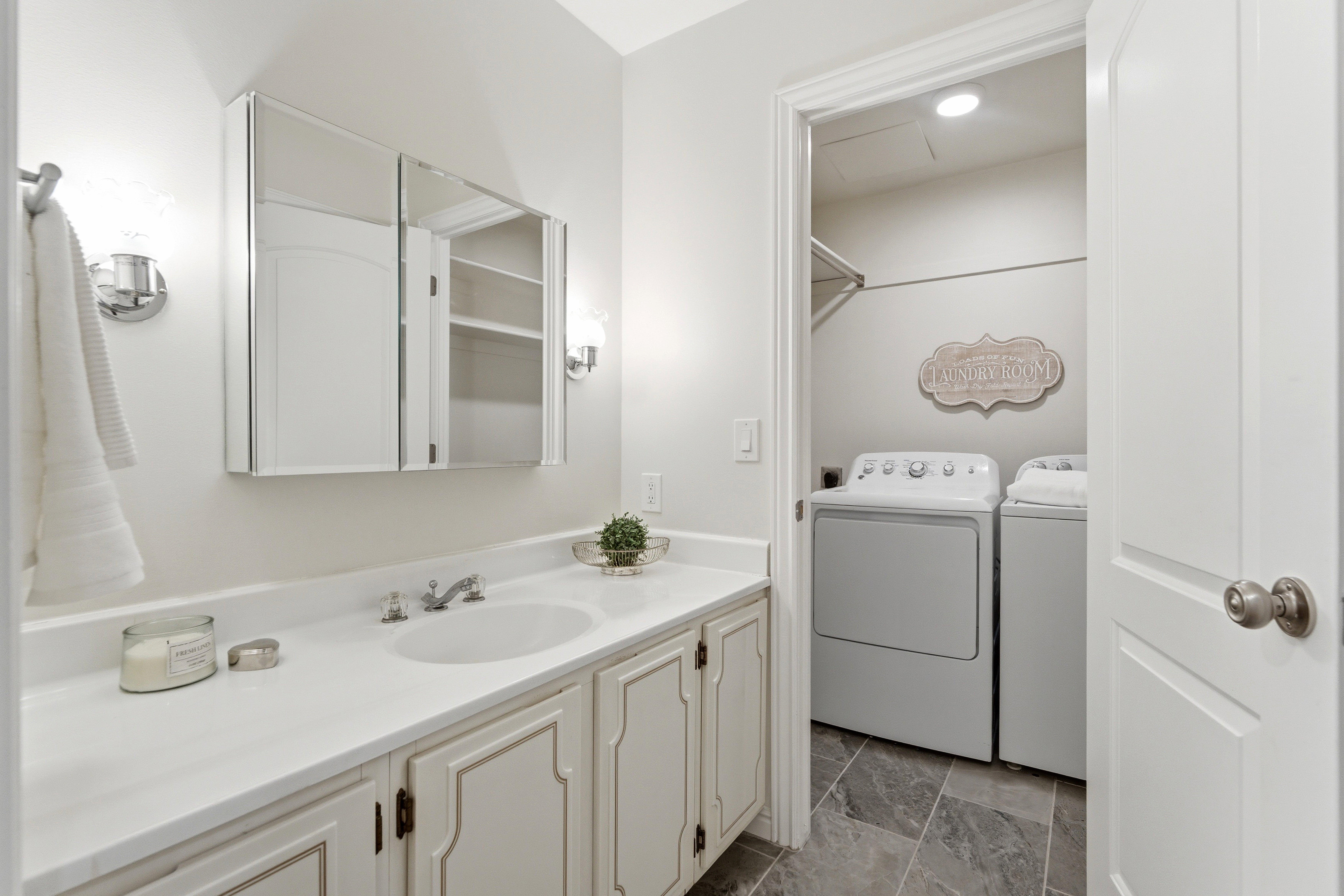 Bathroom vanity with a white countertop and integrated sink, featuring wall-mounted sconces and a mirrored medicine cabinet