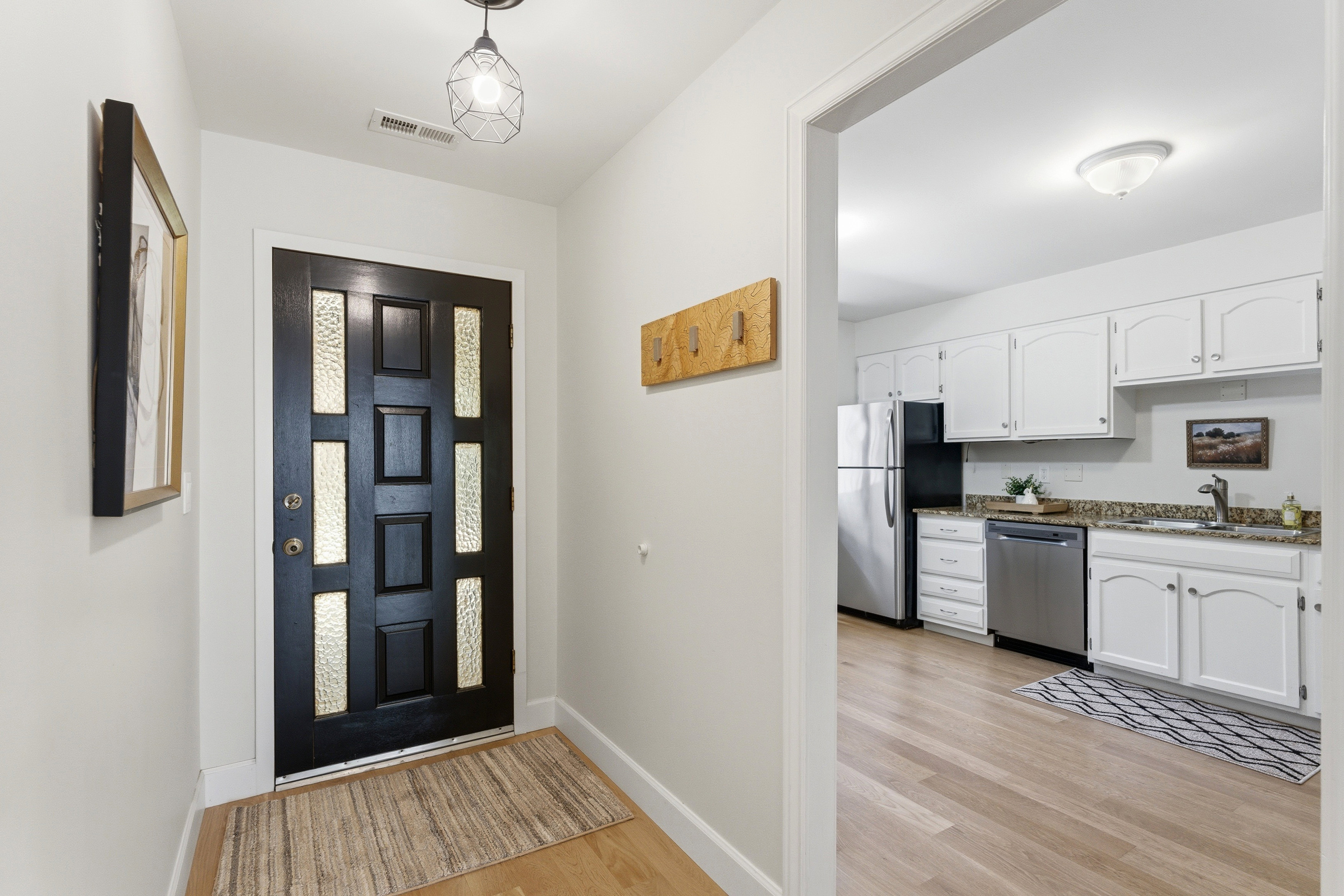 Entryway featuring a paneled black door with frosted glass inserts, wood-finish flooring, and a visible kitchen beyond