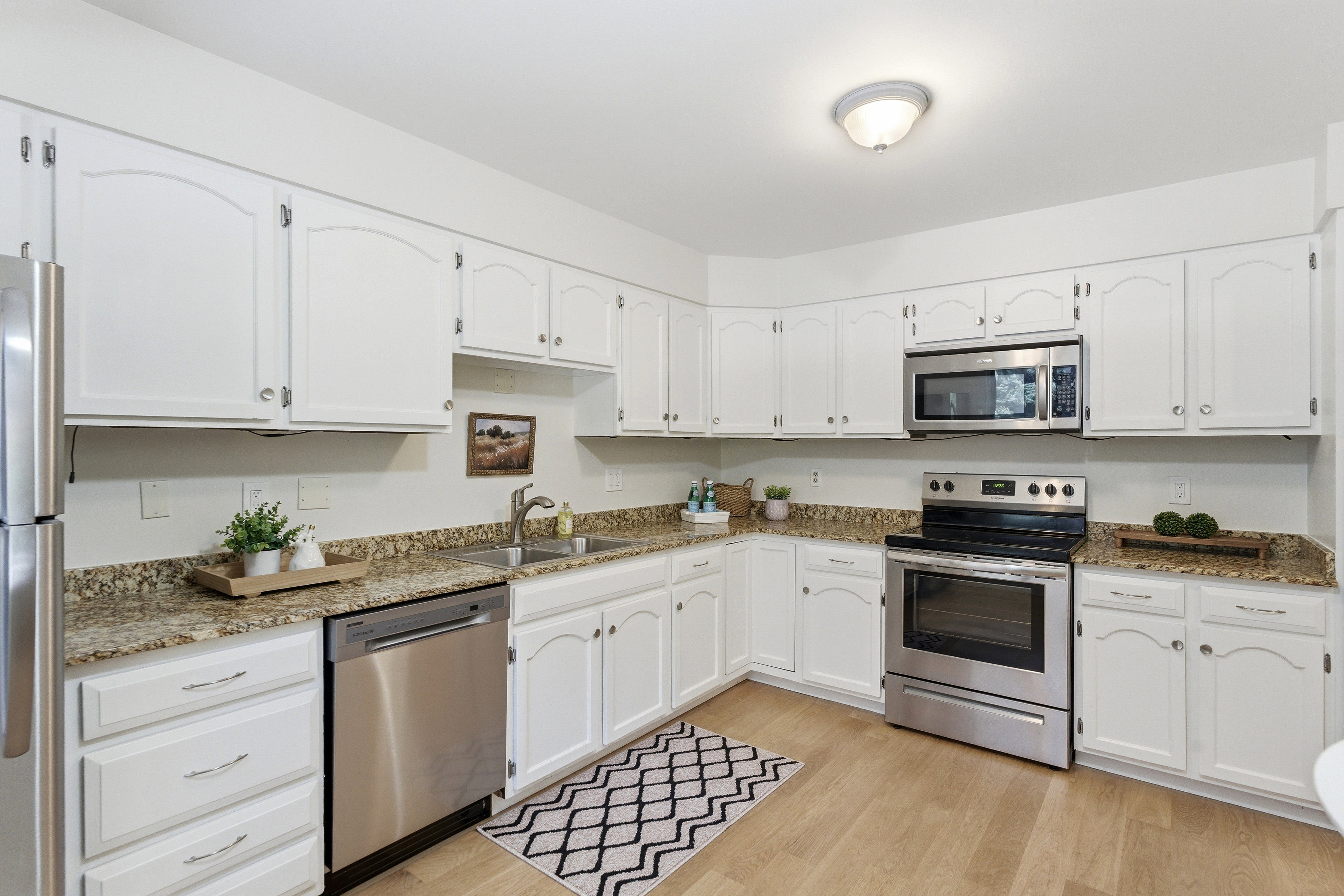 Kitchen featuring white cabinetry, light wood-finish flooring, stainless steel appliances, and speckled countertops