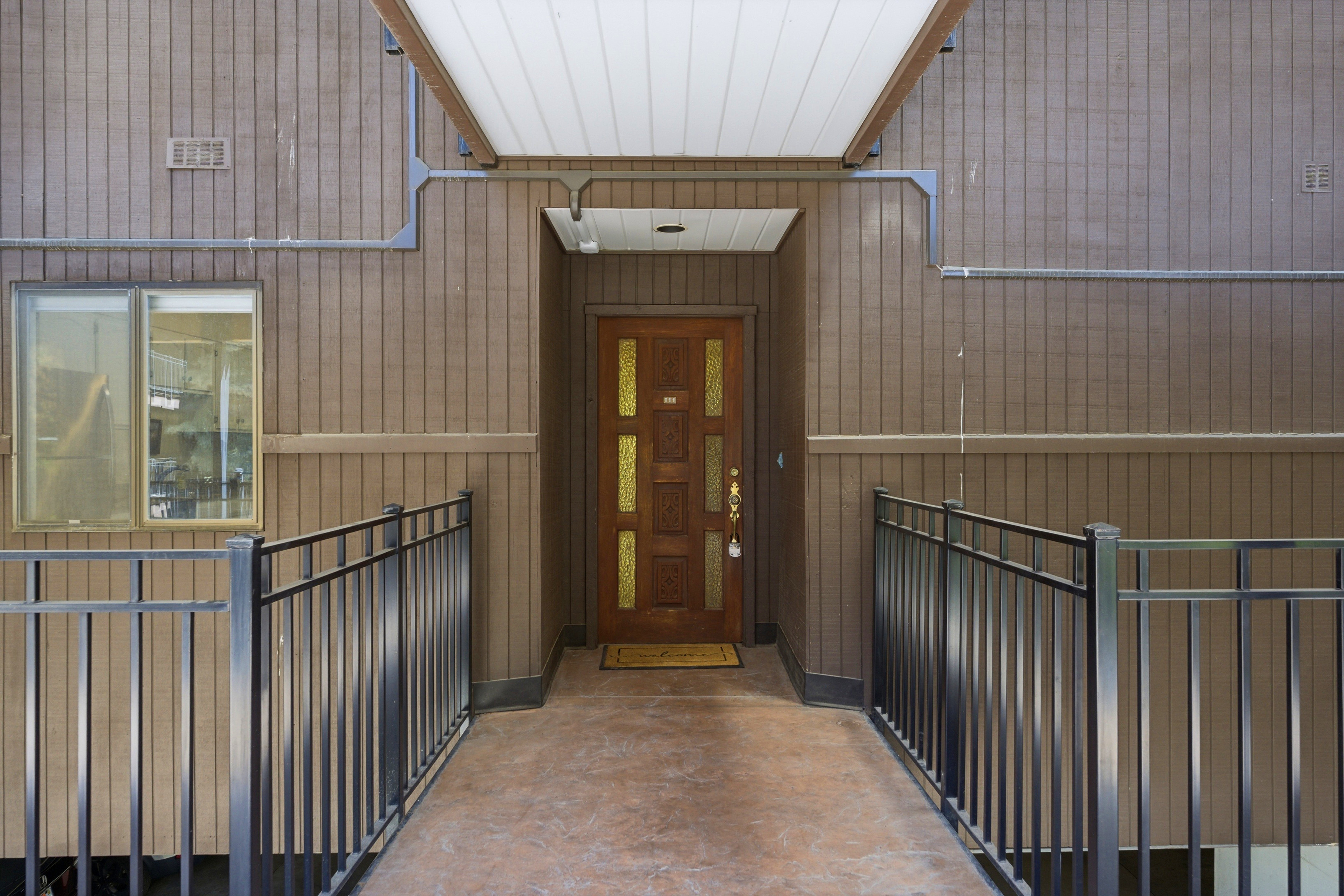 Entryway featuring a wood-panel accent door with decorative brass inserts, sheltered by a white-paneled overhang