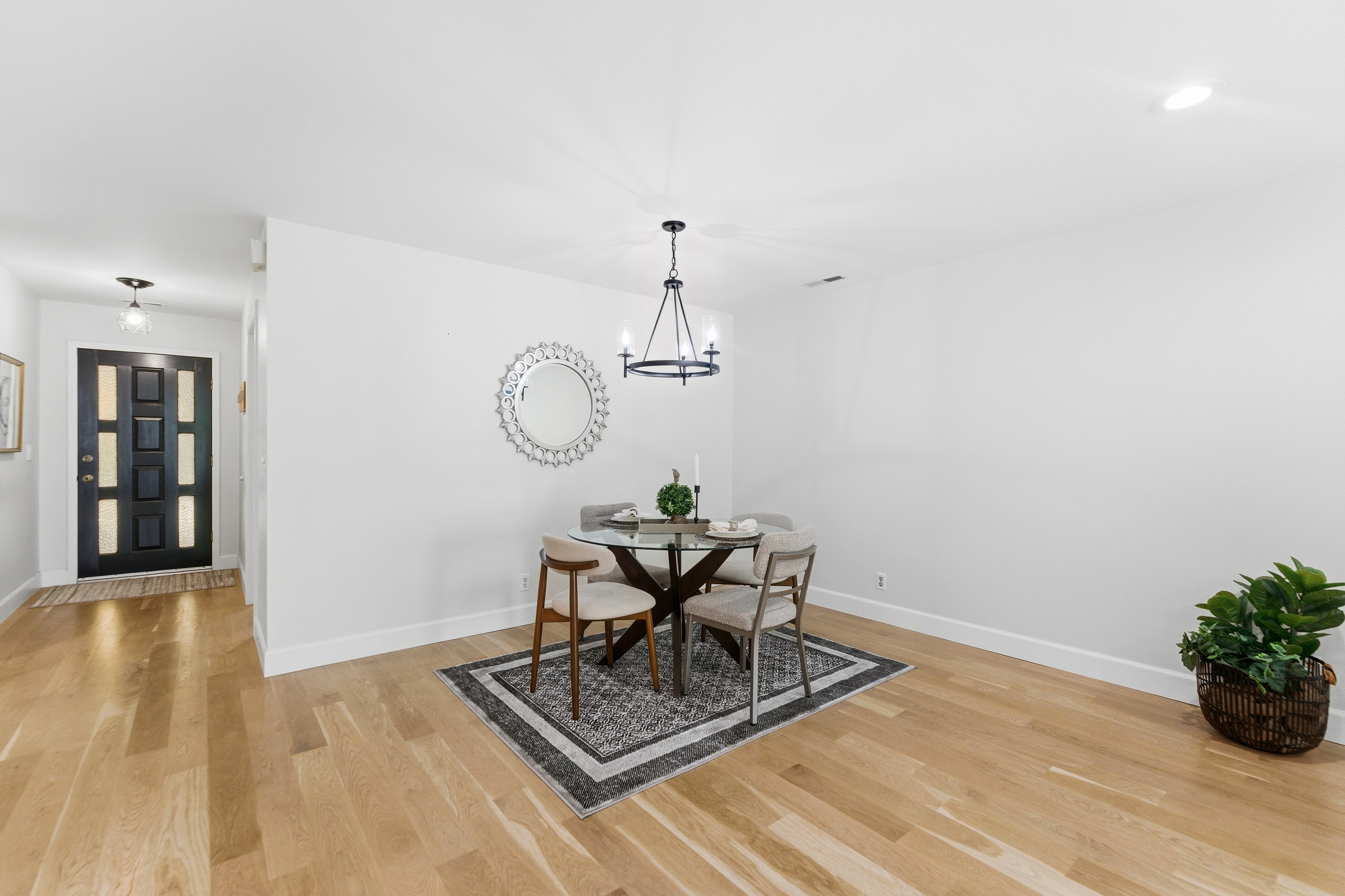 Open-concept living area with light wood-finish flooring, a contemporary chandelier, and a black paneled front door with frosted glass inserts