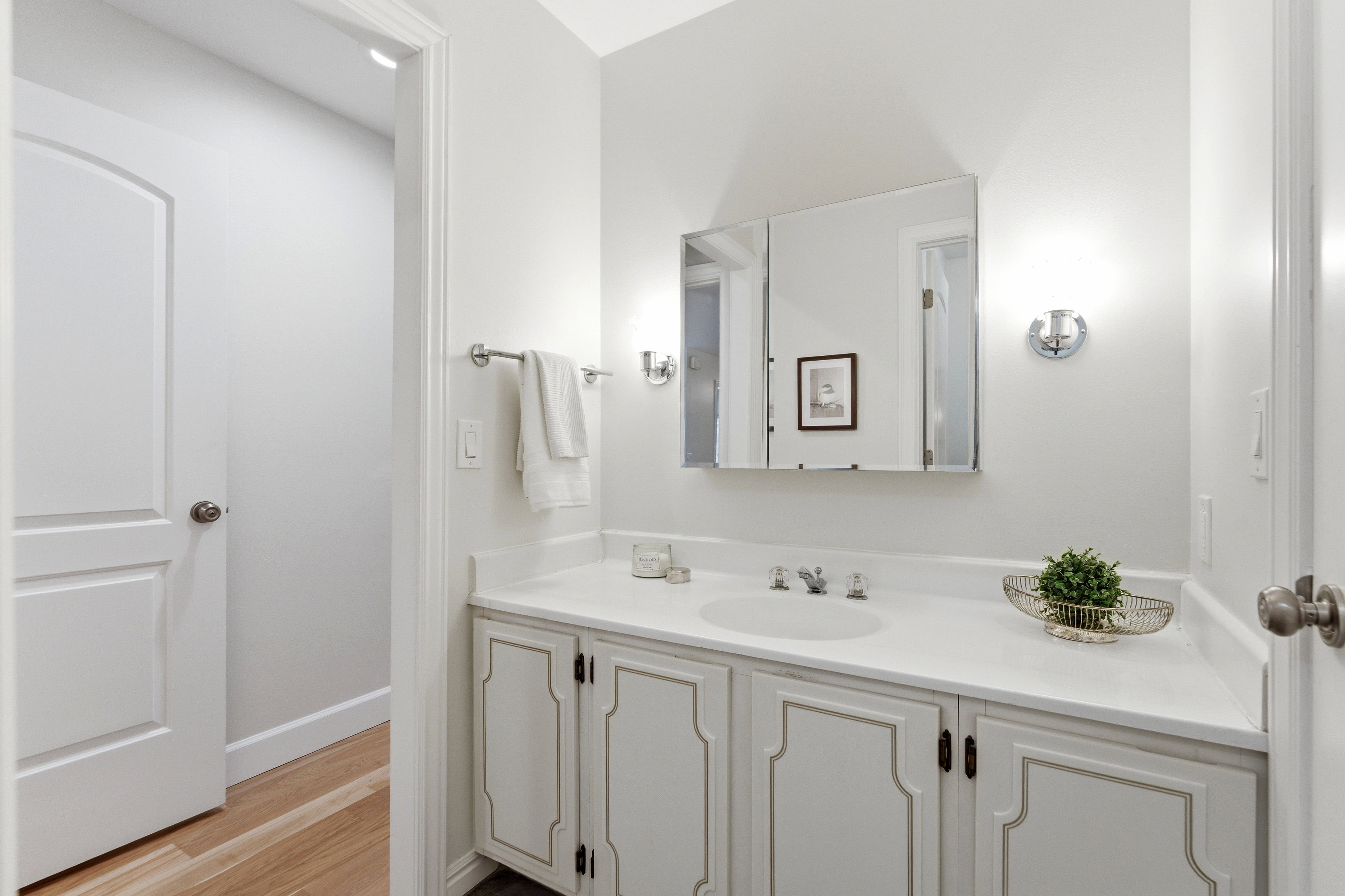 Bathroom vanity featuring a light-colored countertop with an undermount sink, a triple mirrored medicine cabinet, and sconce lighting