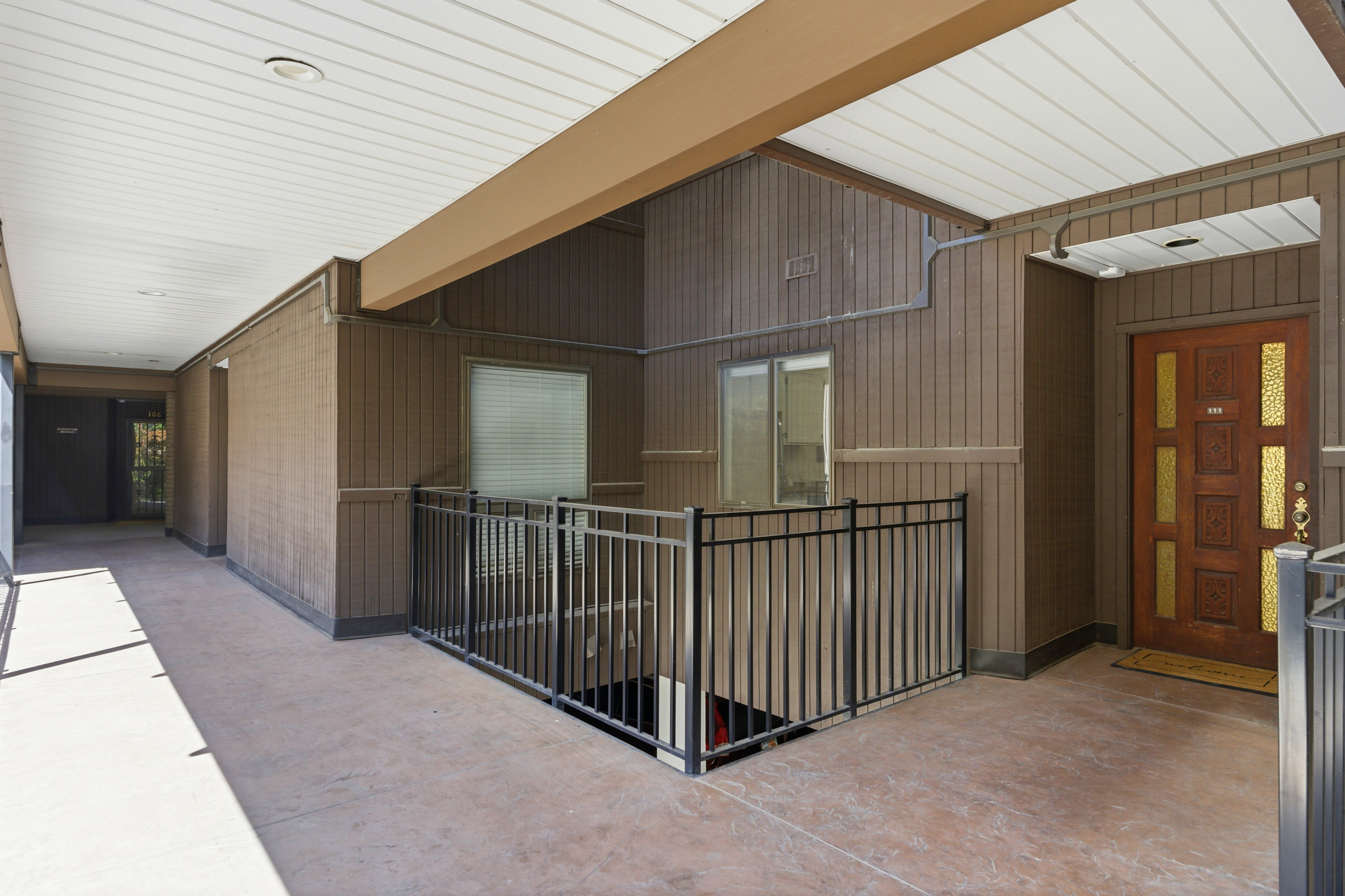 Outdoor entryway featuring a decorative wood entry door with glass inserts, a black metal railing, and a textured concrete walkway