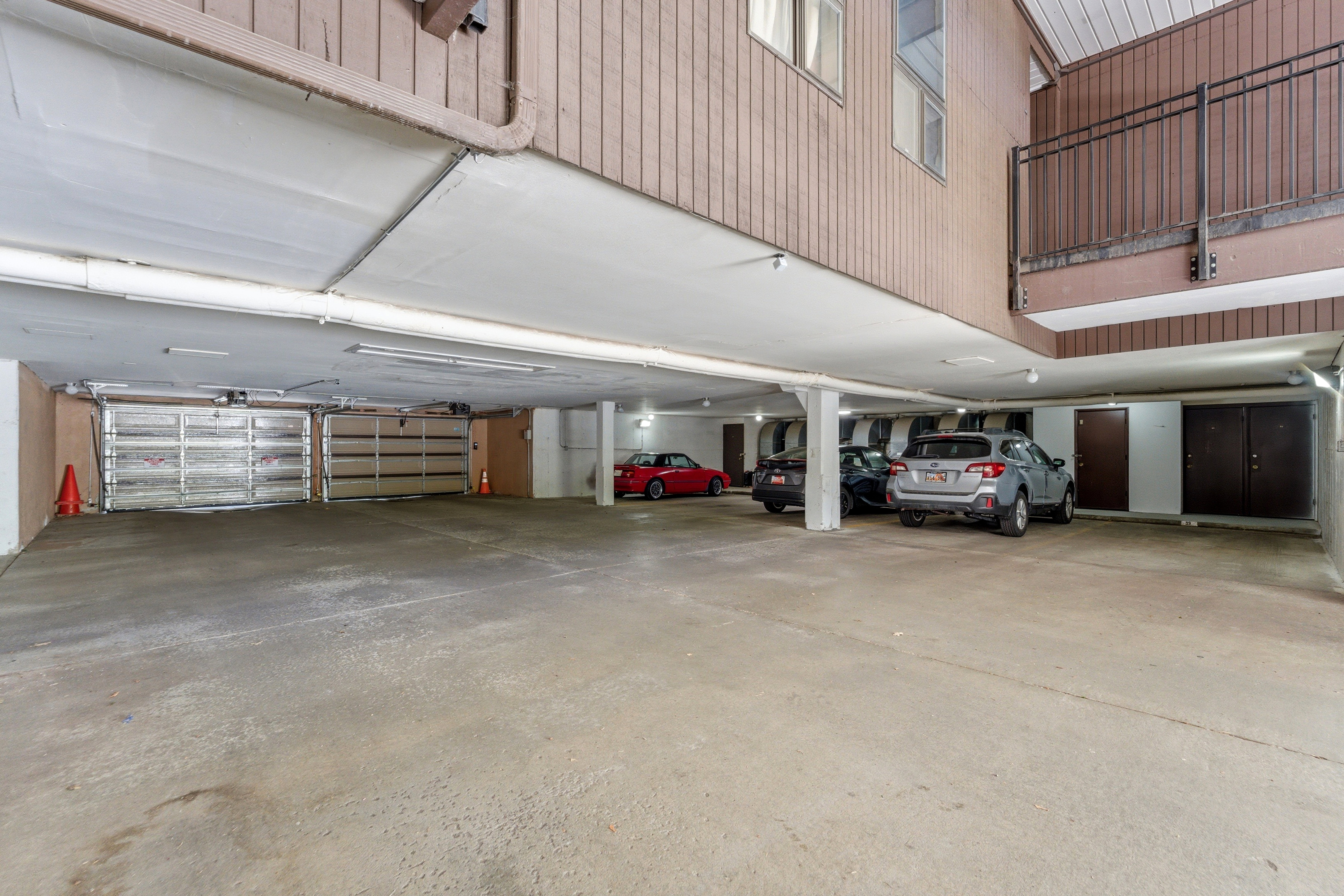 Covered parking area featuring a concrete floor, multiple support columns, and fluorescent overhead lighting