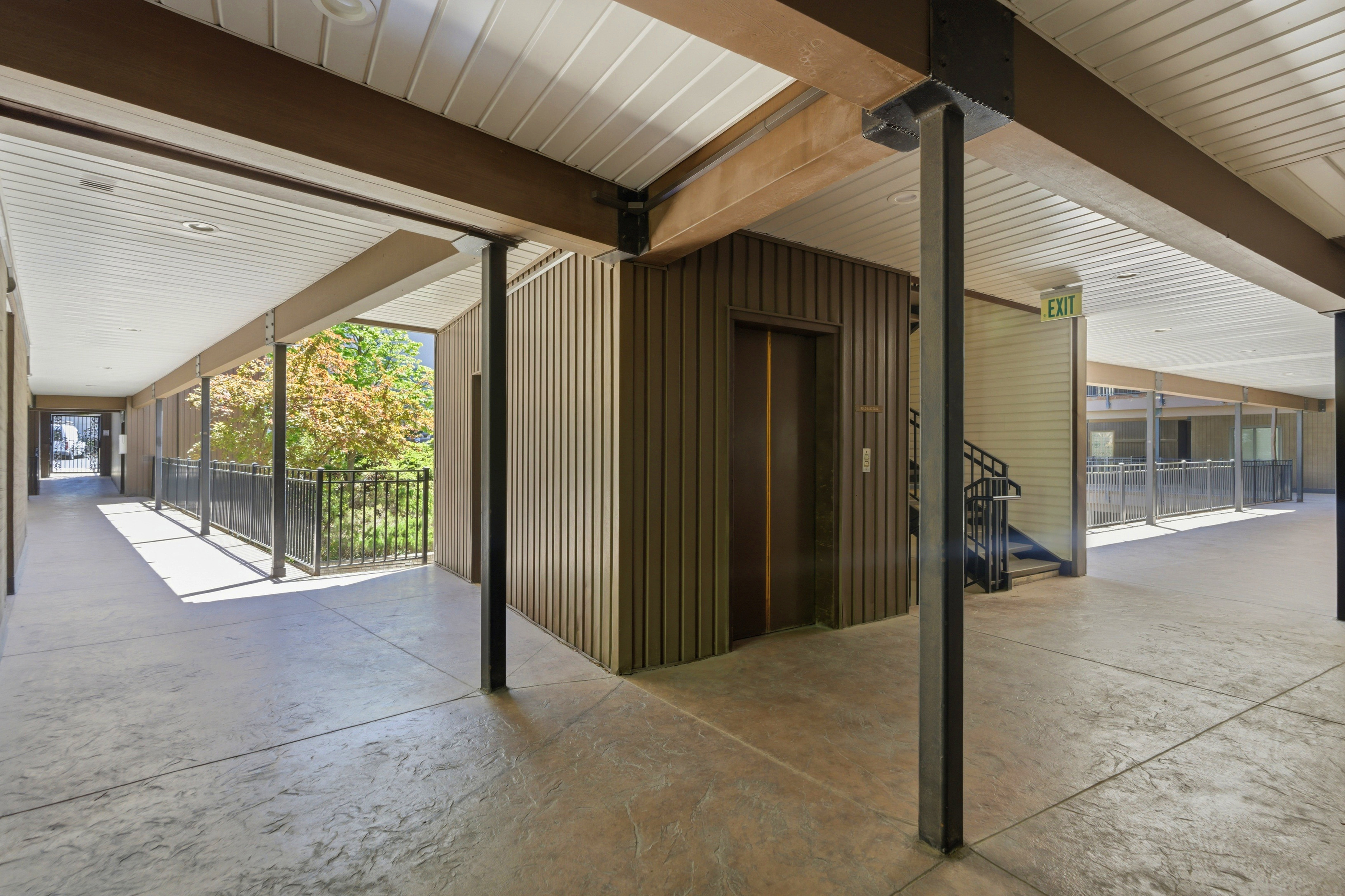 Building hallway featuring an elevator, textured concrete flooring, and metal railings