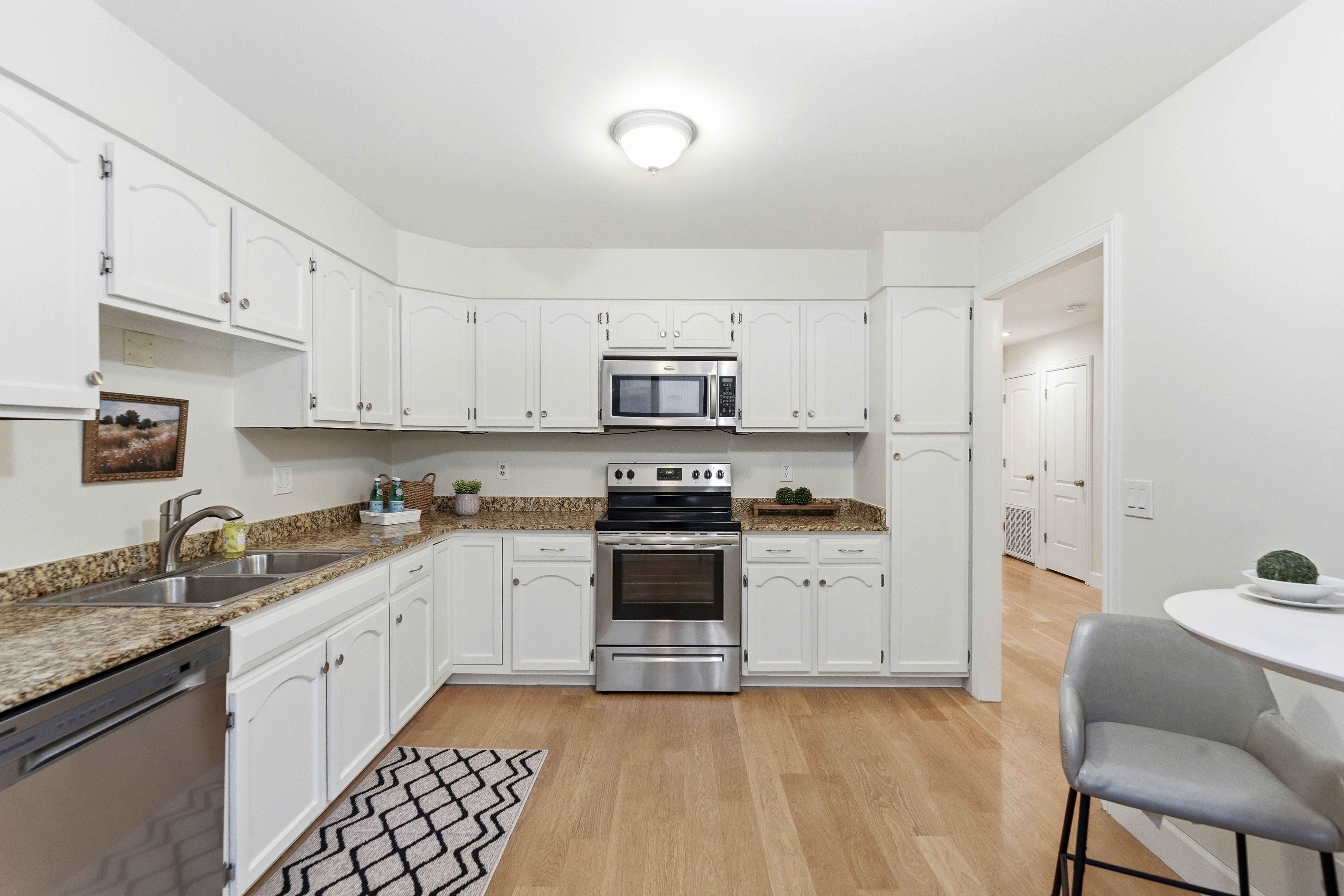 U-shaped kitchen featuring white cabinetry, stainless steel appliances, speckled stone countertops, and wood-finish flooring