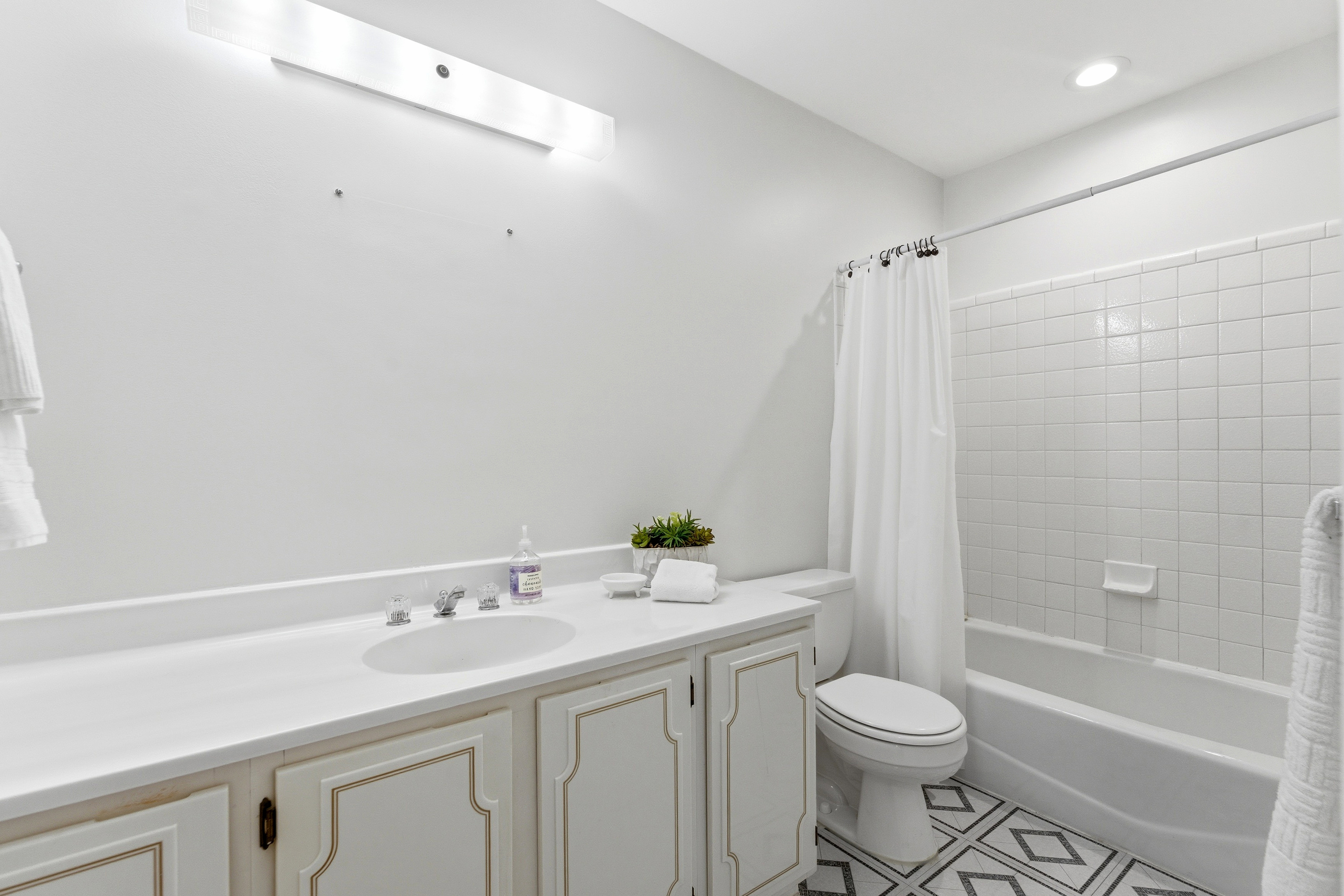 Bathroom featuring a white vanity with an integrated sink, polished chrome faucet, white countertop, and patterned floor tile