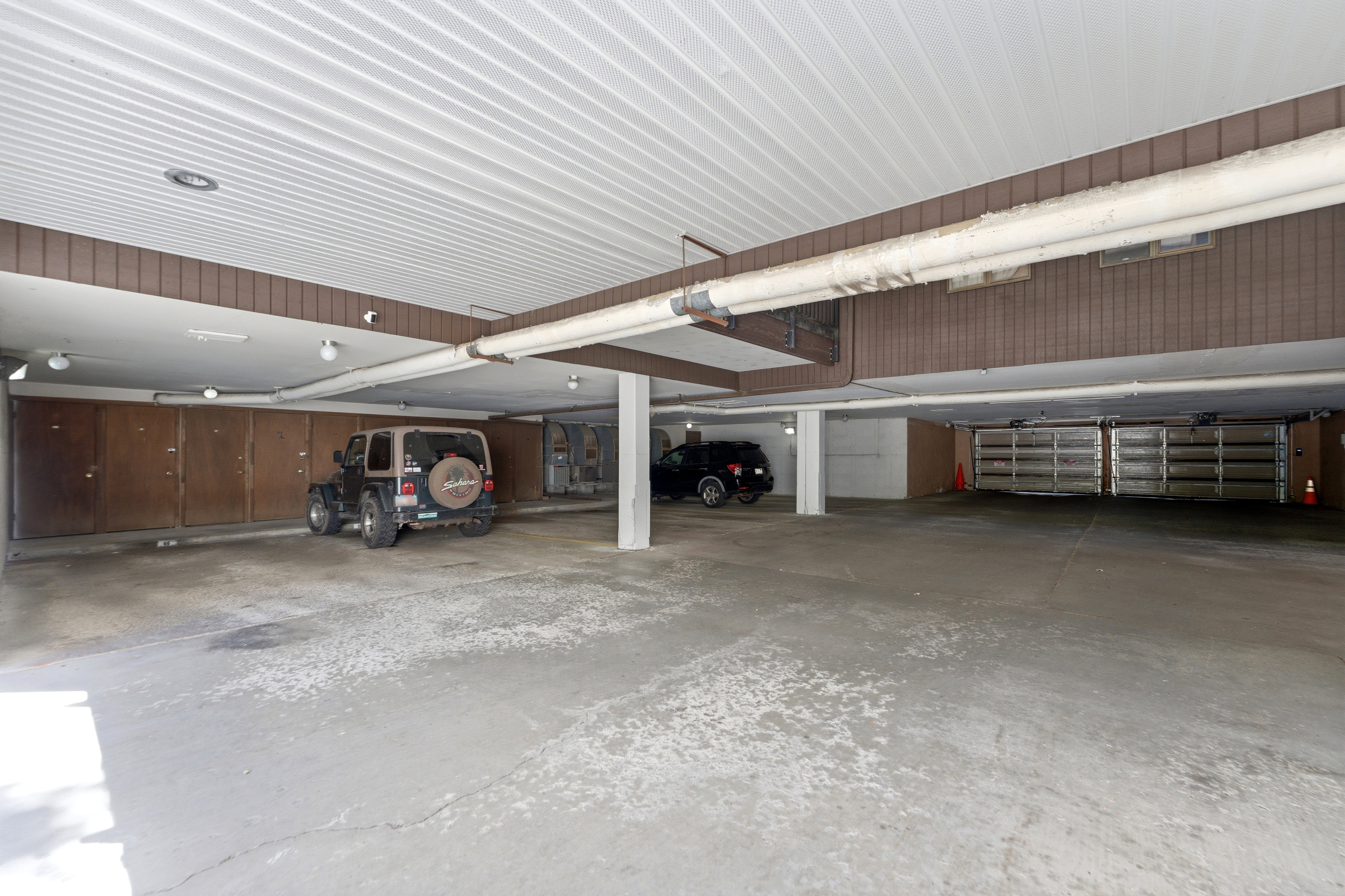 Spacious underground parking garage featuring a concrete floor, corrugated metal ceiling, and individual storage units with wood-panel doors
