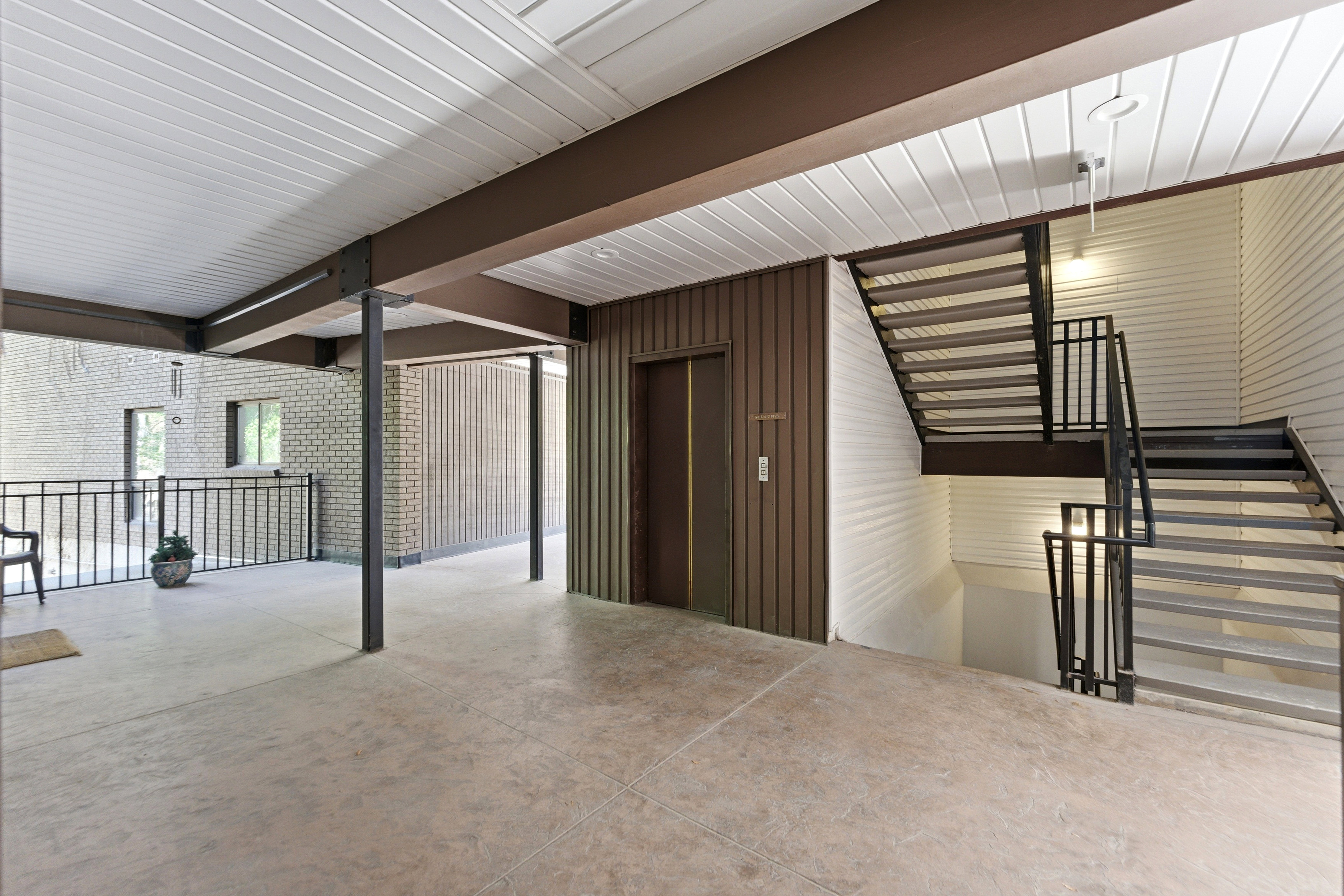 Covered outdoor corridor featuring structural beams, textured flooring, and a black iron railing