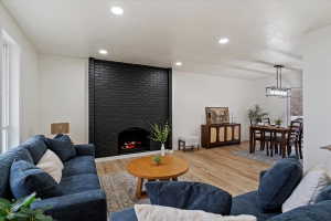 Living area featuring a black brick fireplace with an arched opening, recessed lighting, wood-finish flooring, and a dining area with a linear chandelier